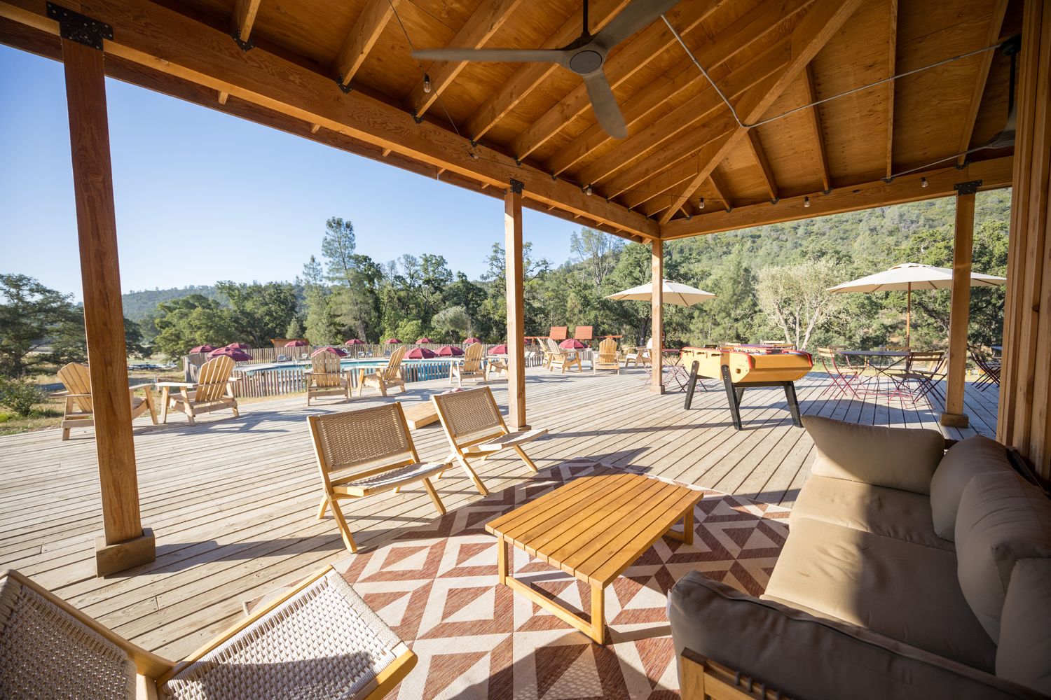 Covered outdoor deck with wooden furniture overlooking resort pool area.