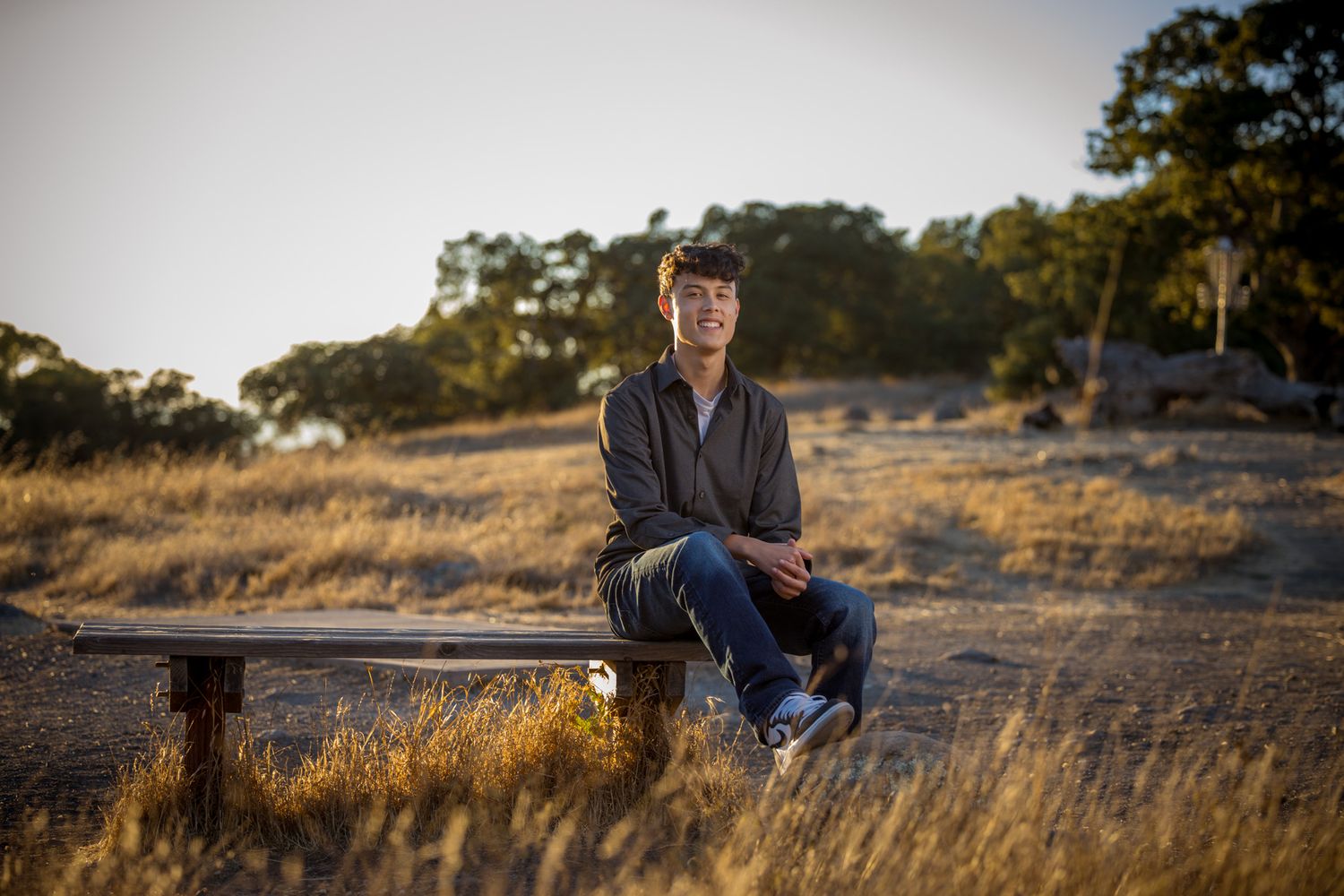 Senior Photos - Sunset portrait of someone seated on a wooden bench in natural setting.