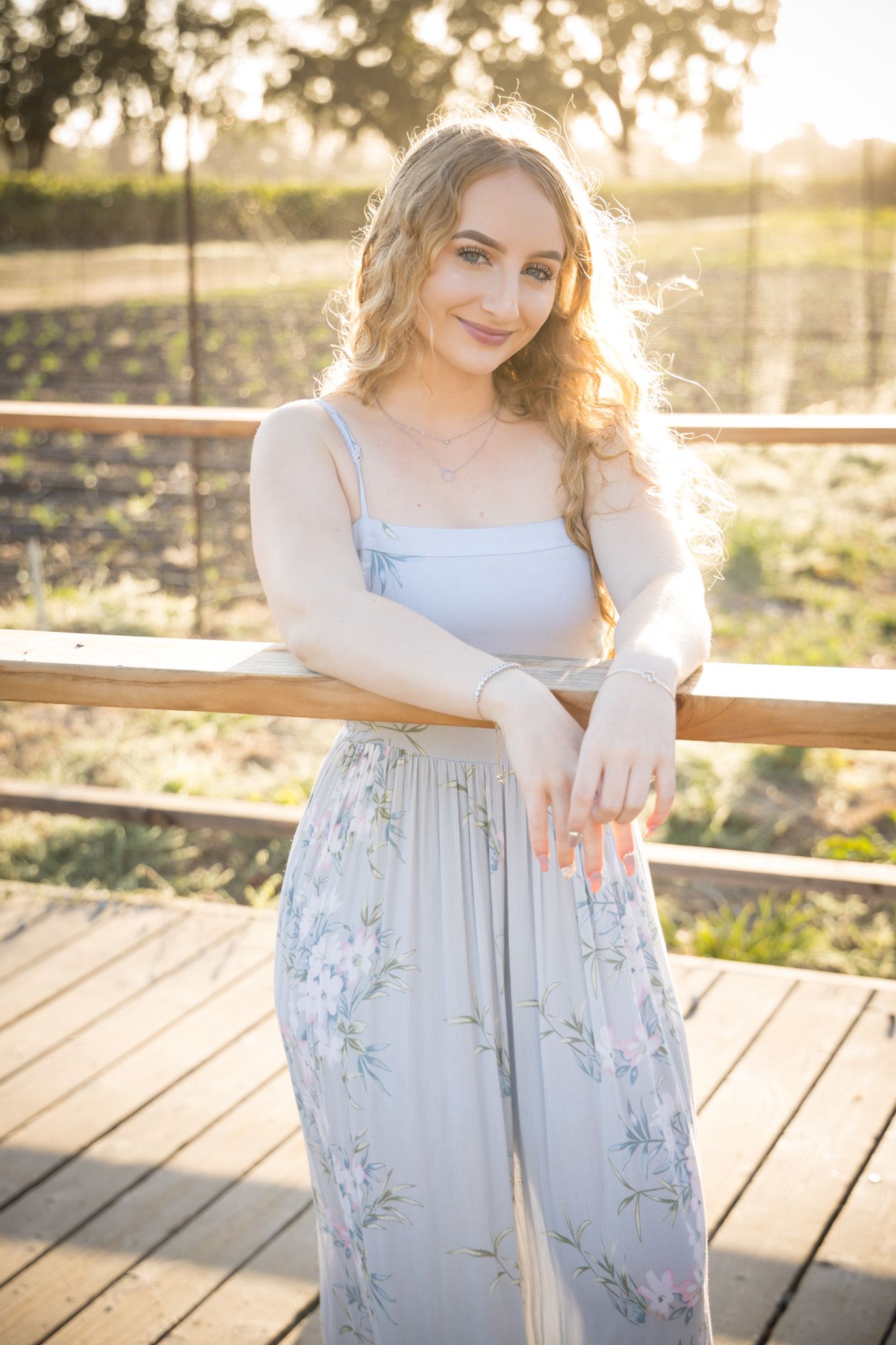 Sunlit portrait of person in floral overalls and white top on wooden deck during golden hour.