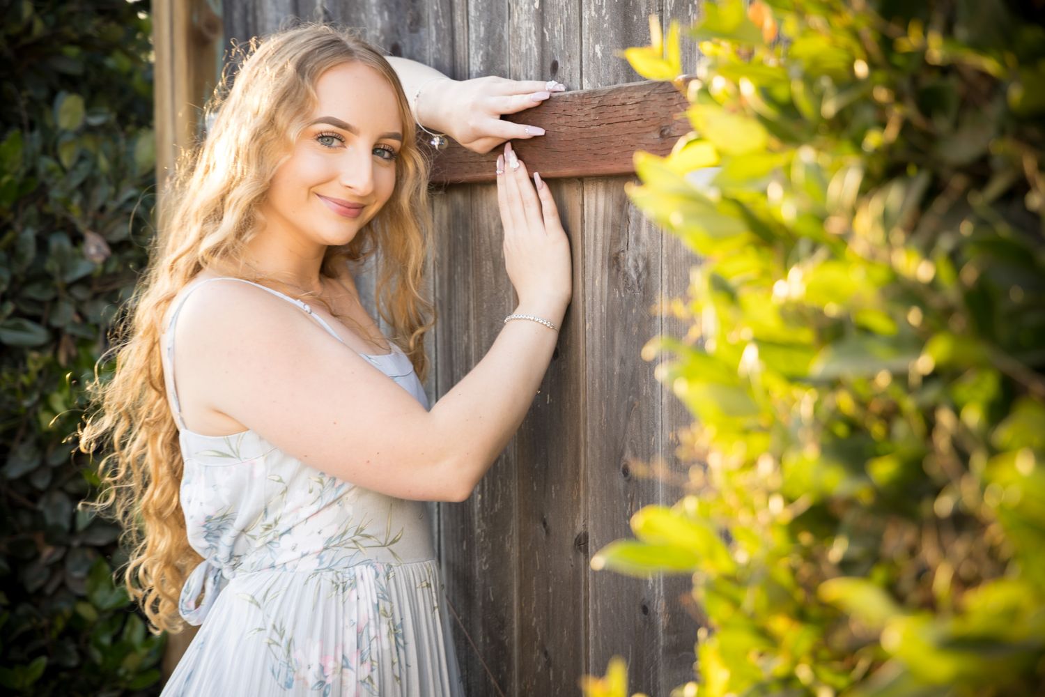 A light and airy portrait in a garden setting with soft lighting and wooden fence backdrop.