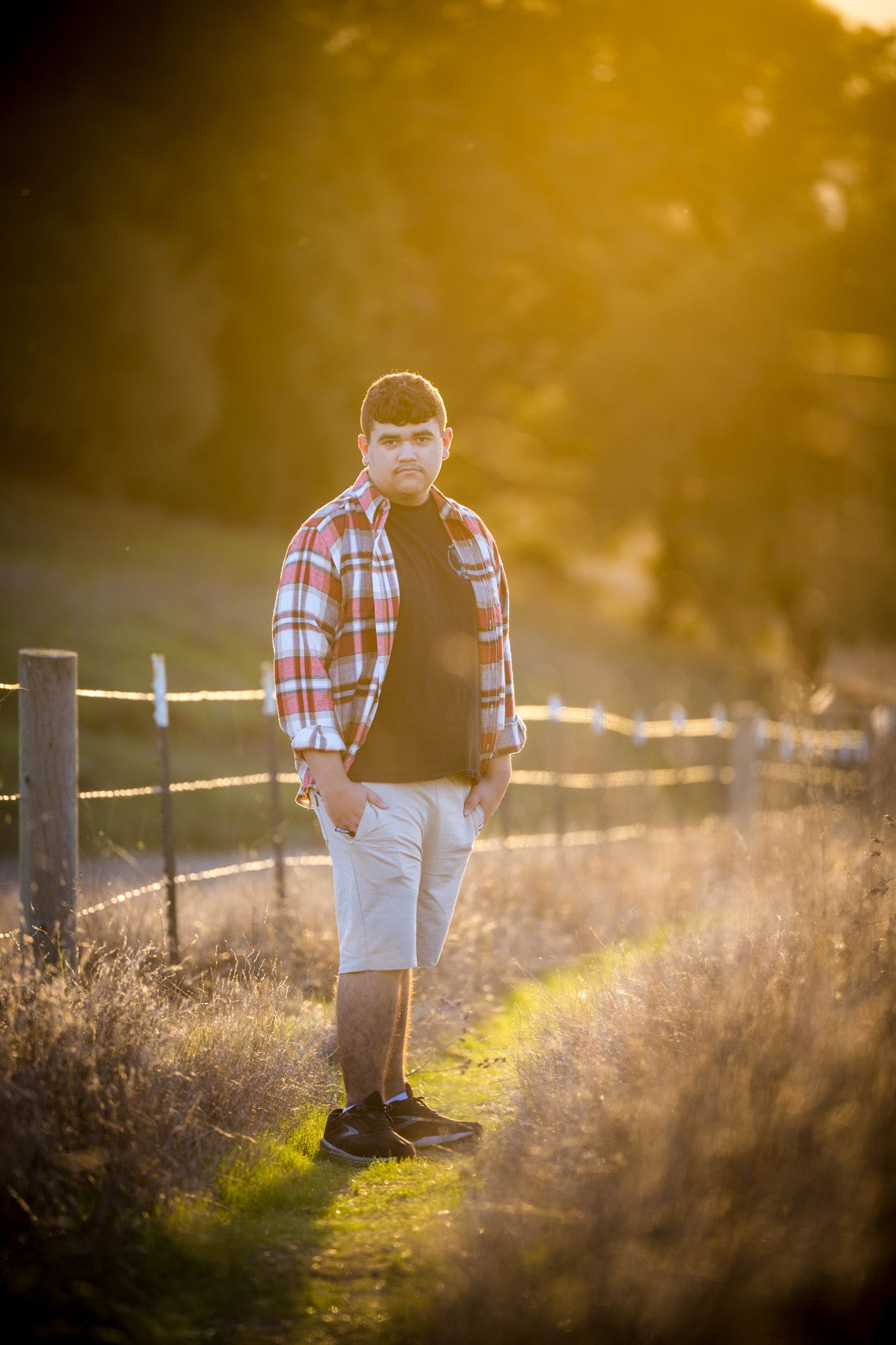 Casual portrait along fence-lined trail during golden hour sunset.