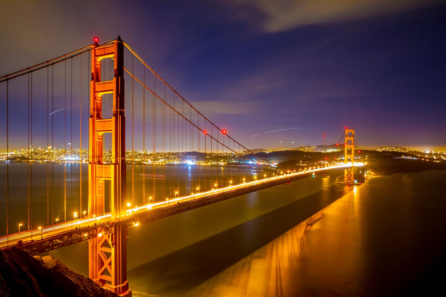 Iconic Golden Gate Bridge glowing orange at night with San Francisco city lights in the background.