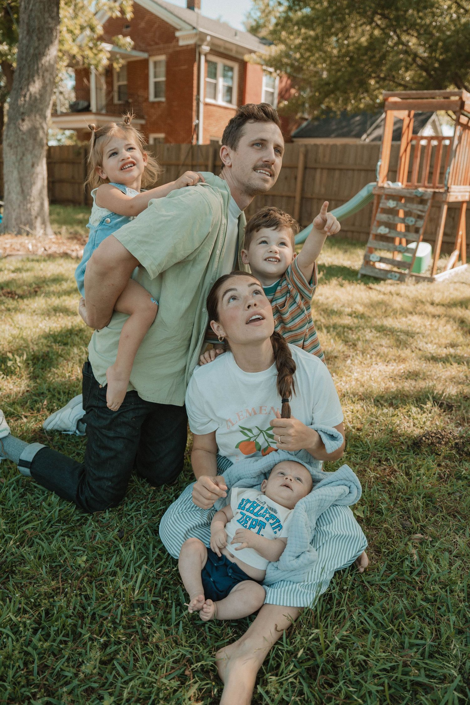 Family lounging together on grass in backyard during golden hour.