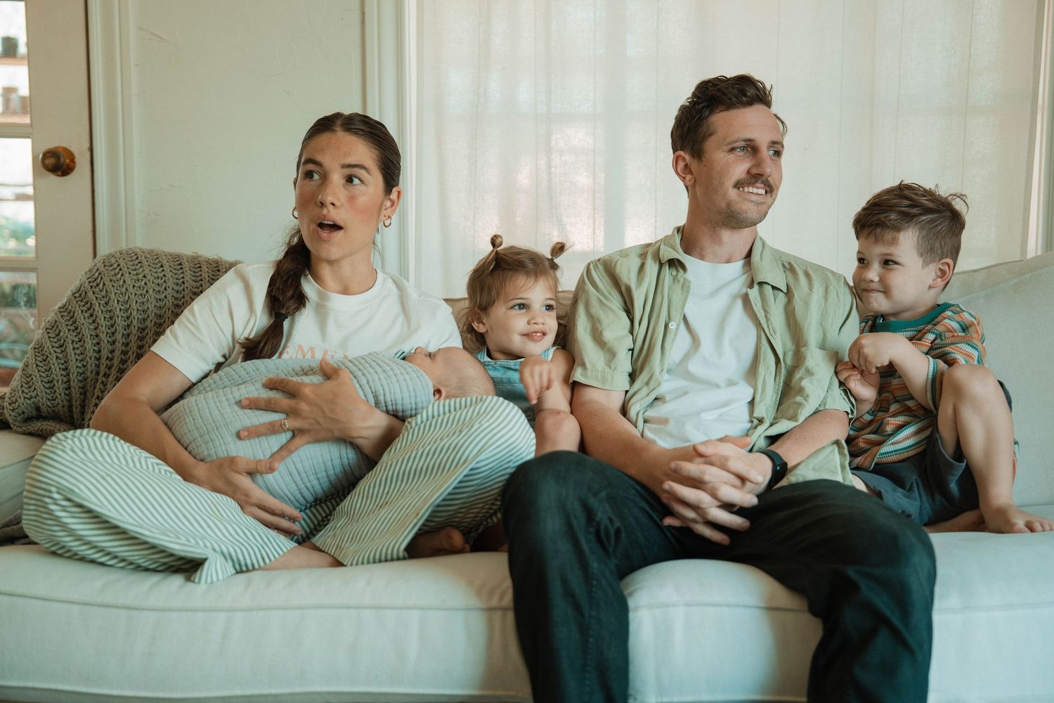Joyful family lounging on light blue couch with guitar and children.