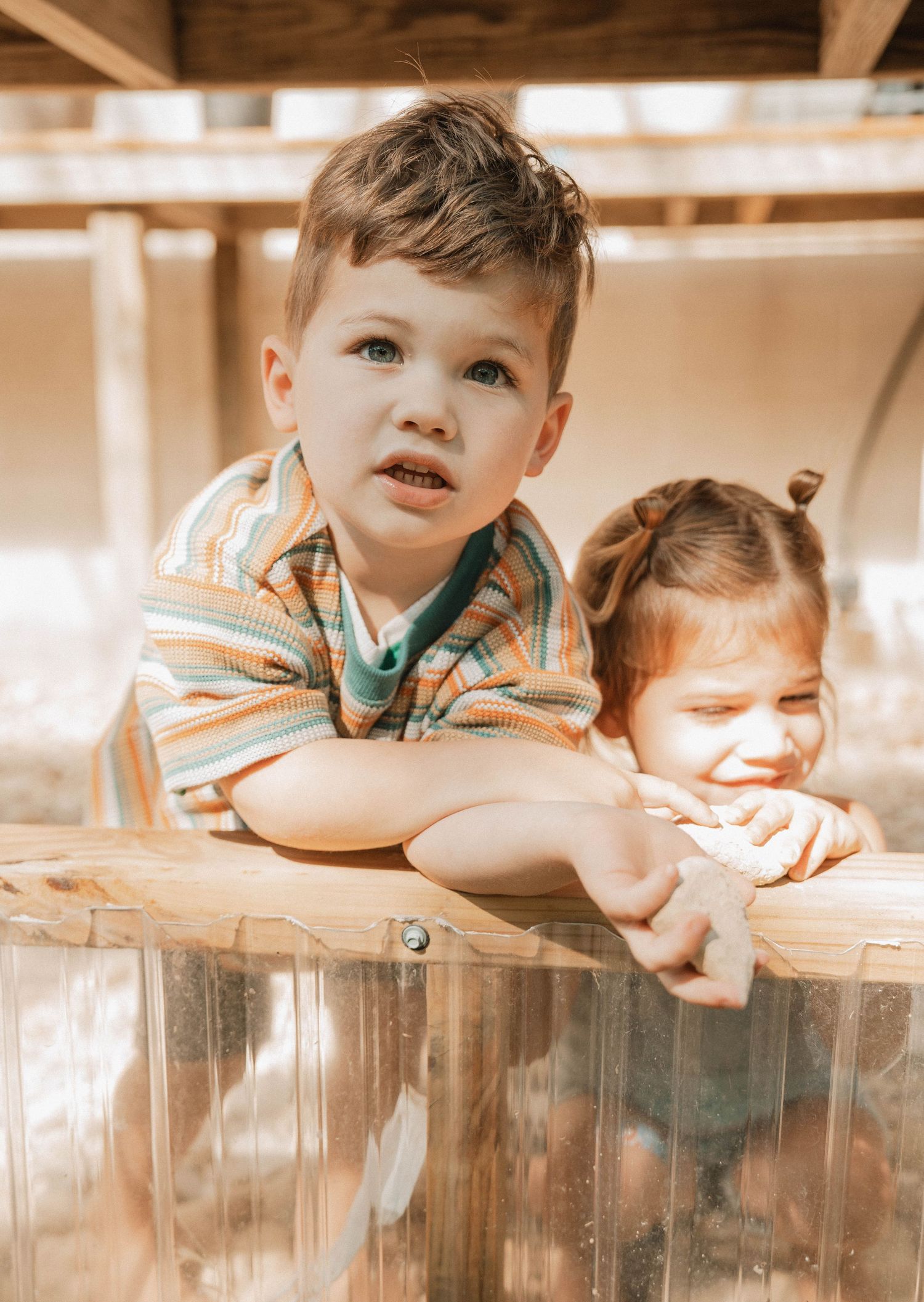 Child peering curiously over a wooden surface in warm lighting.