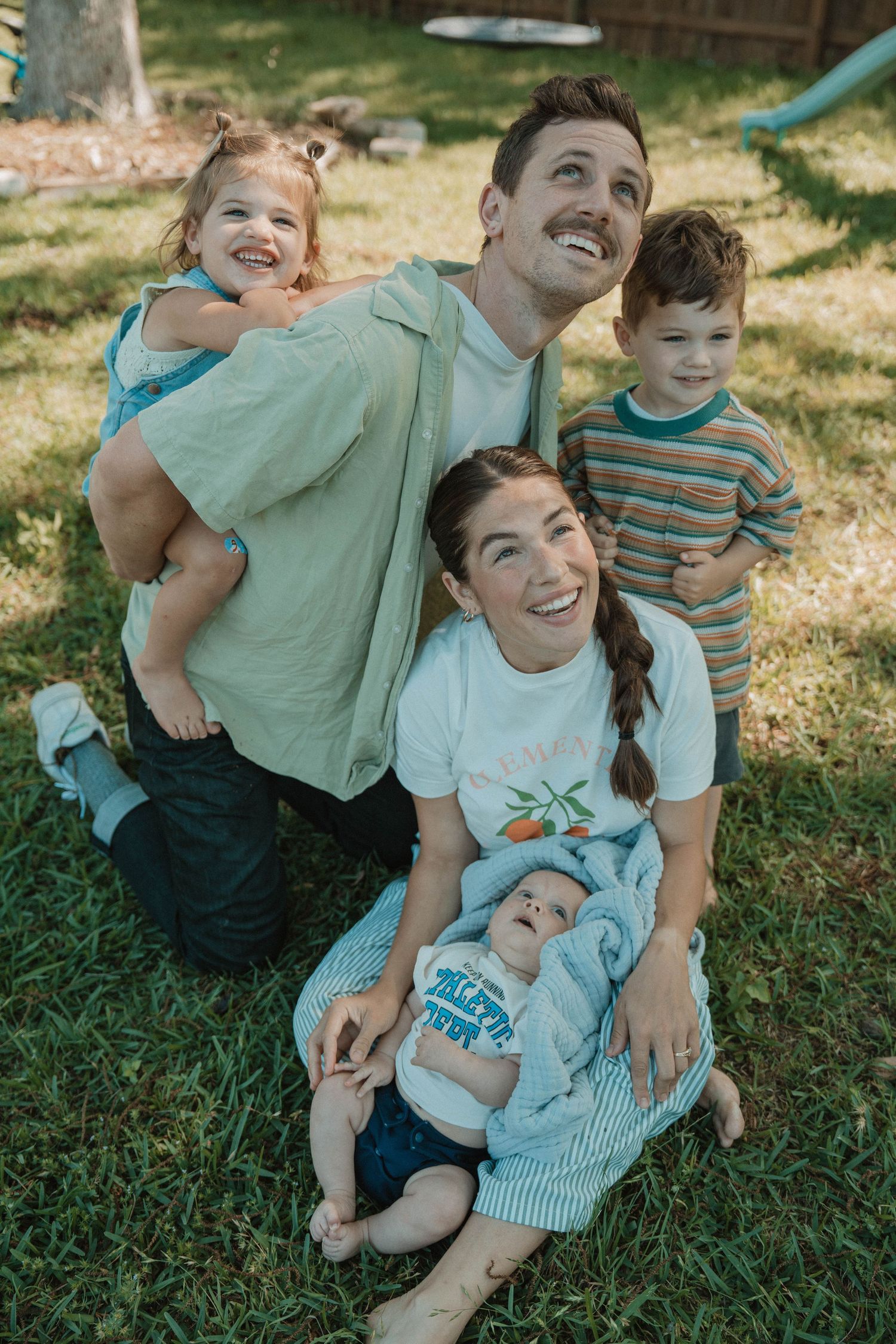 Family enjoying playful moments together on green grass in a backyard setting.