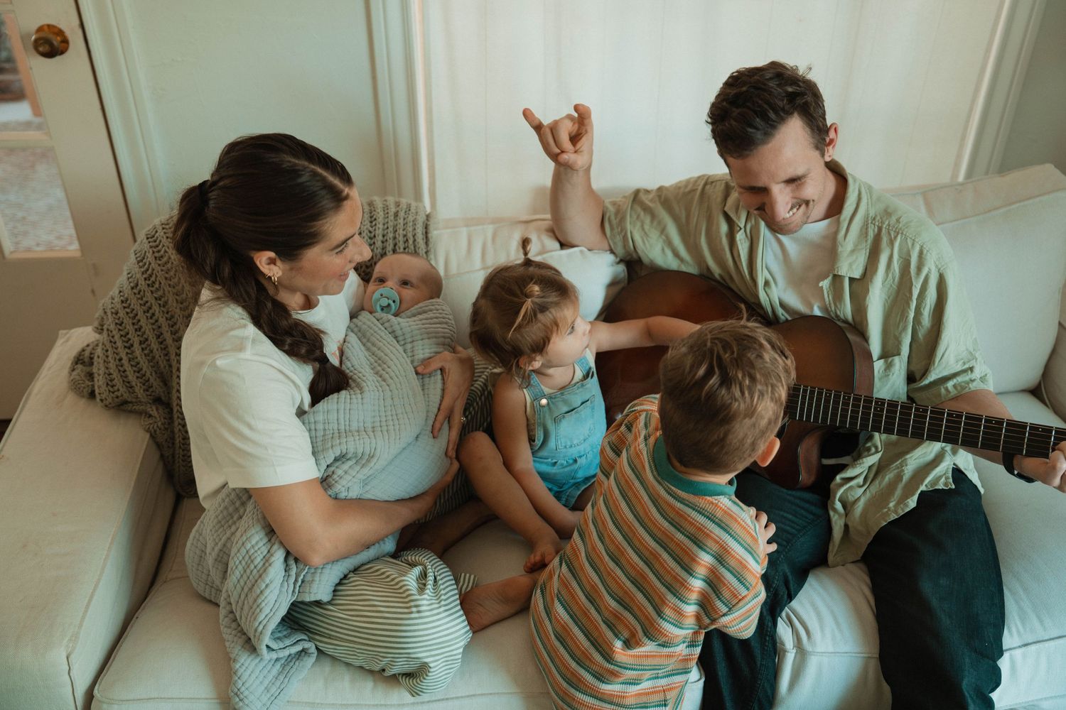 Candid family moment on couch with guitar and children enjoying music together.