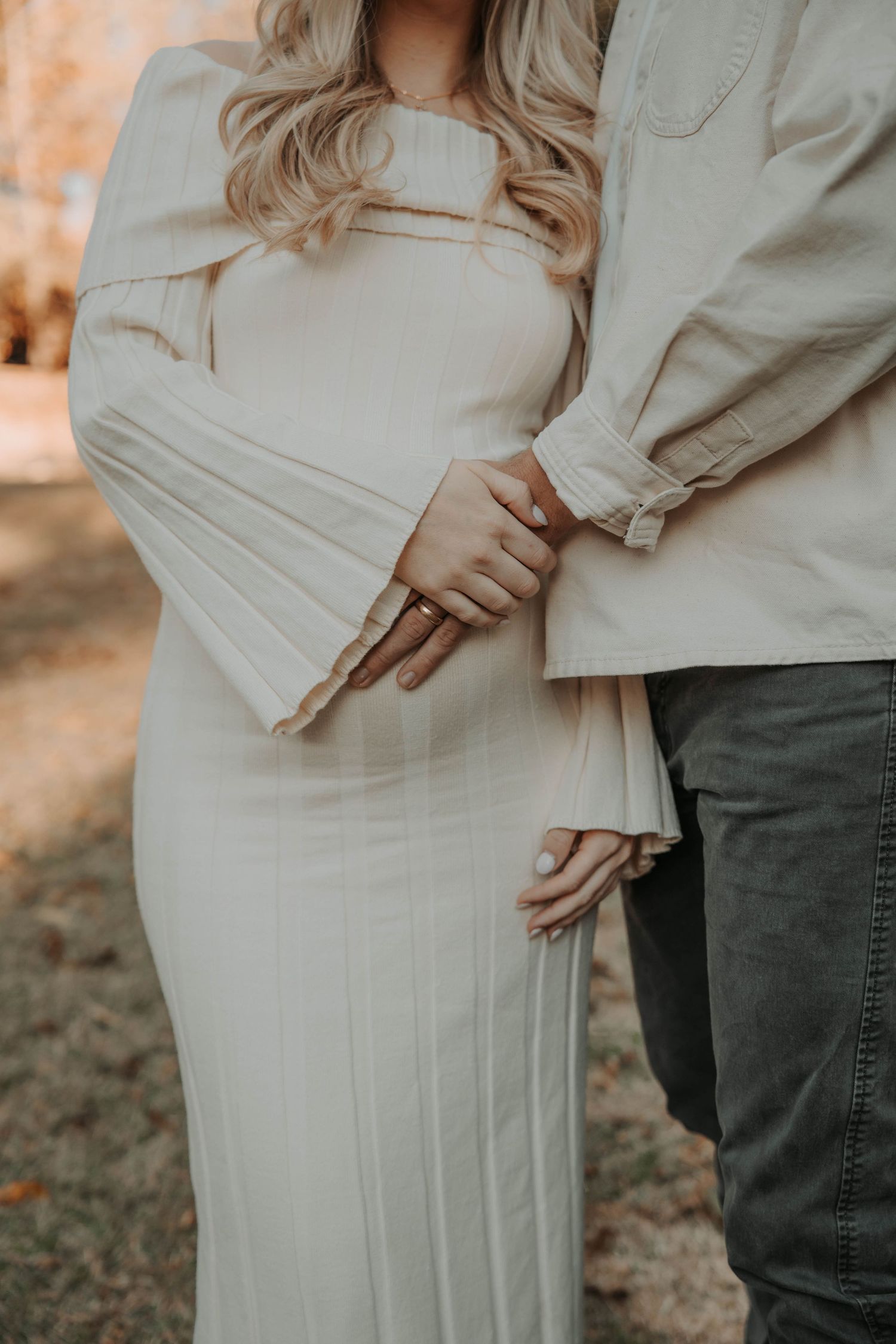 A couple in casual attire embracing outdoors during an autumn maternity photoshoot.