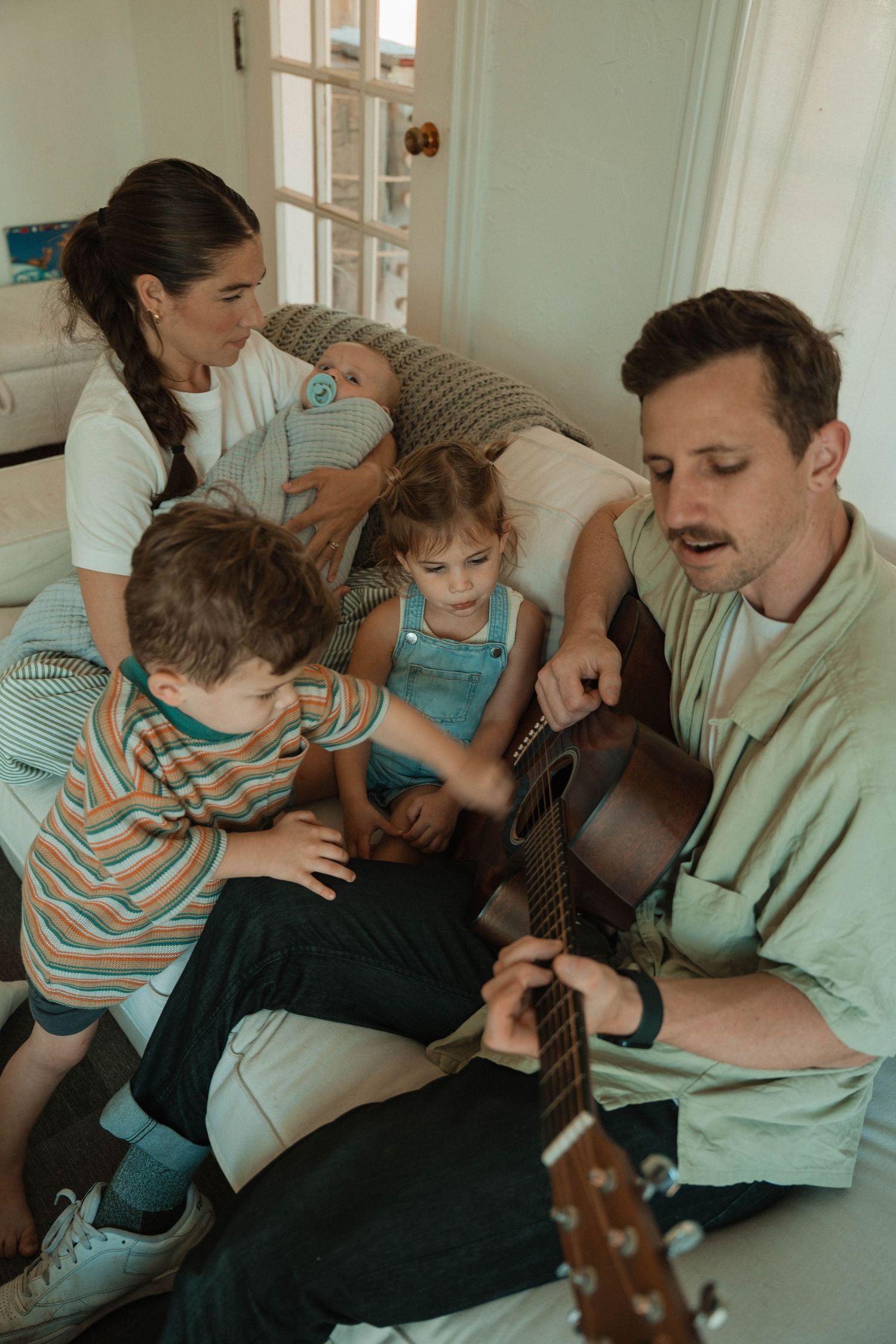 Intimate family music session with acoustic guitar on couch.