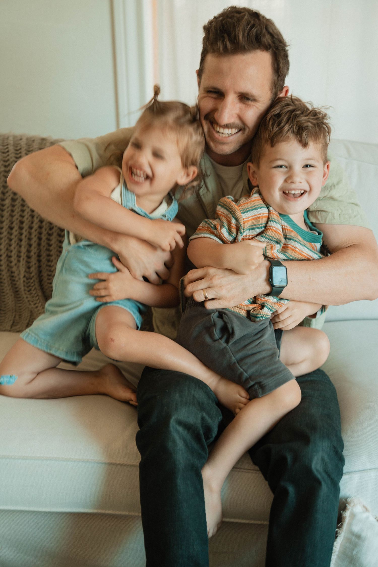 Playful family cuddle session on a comfortable gray couch.
