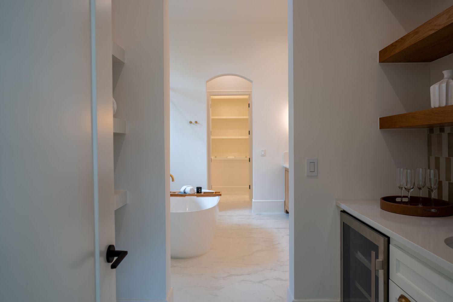 White corridor leading to bathroom with arched doorway and built-in storage.