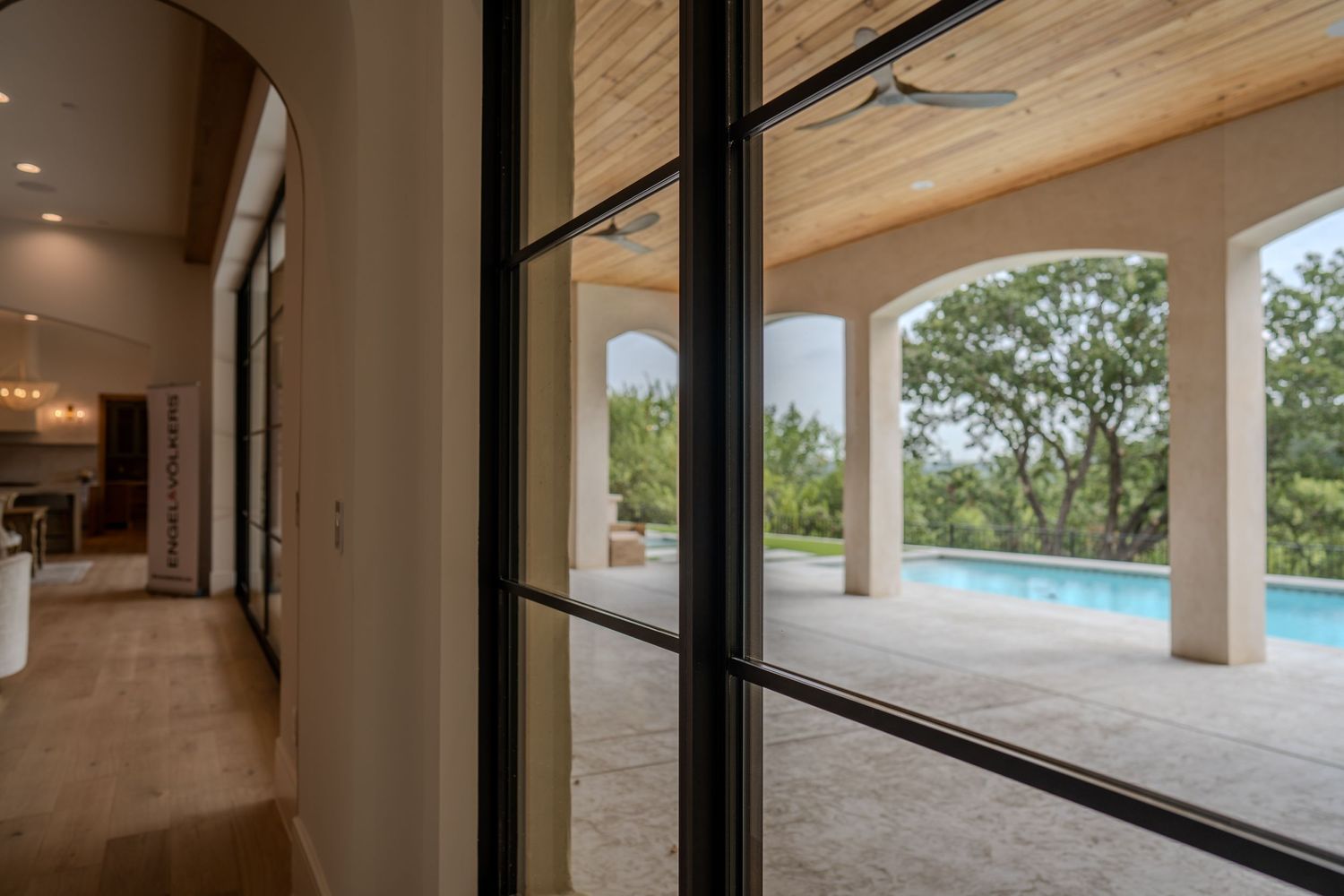 Modern hallway with floor-to-ceiling windows overlooking a luxurious pool and outdoor patio area.