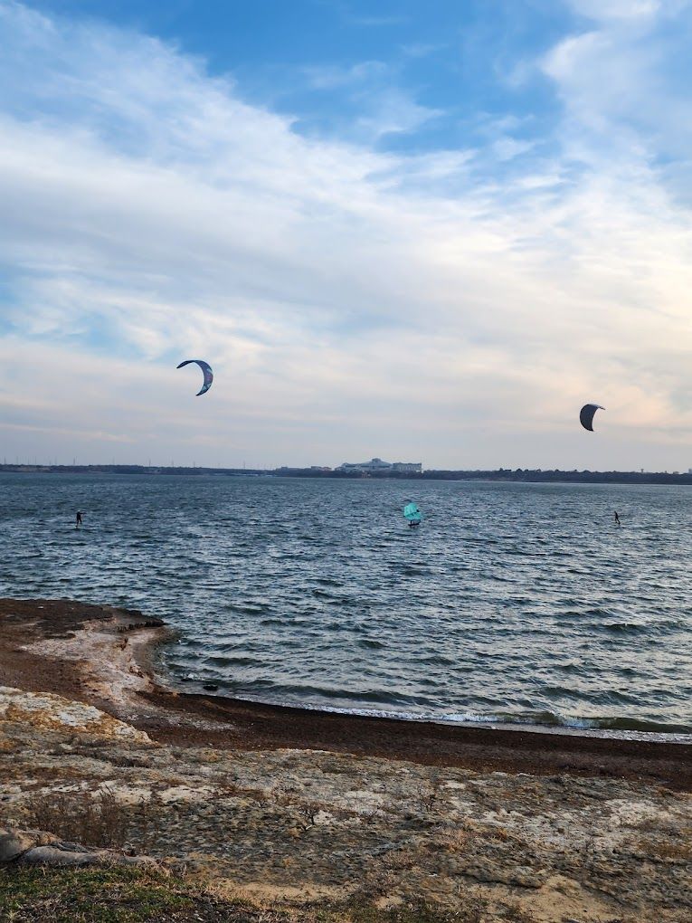 Kitesurfers glide across choppy waters on a rocky coastline under a dramatic cloudy sky.