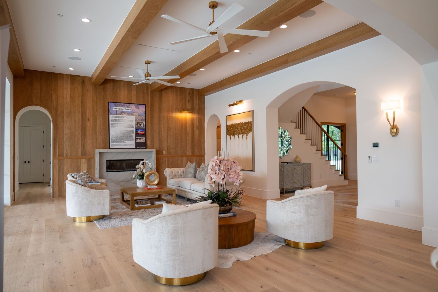 Elegant living room with wooden beam ceiling, white curved chairs, and arched doorways.