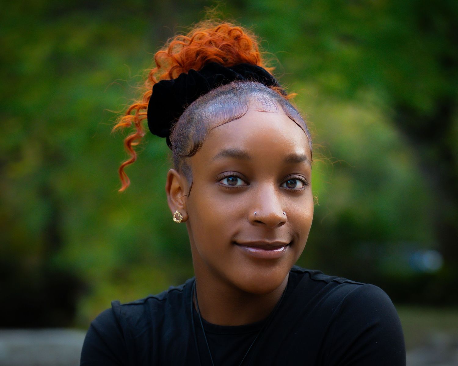 Portrait of a person with vibrant orange hair and a headband against a blurred green background.