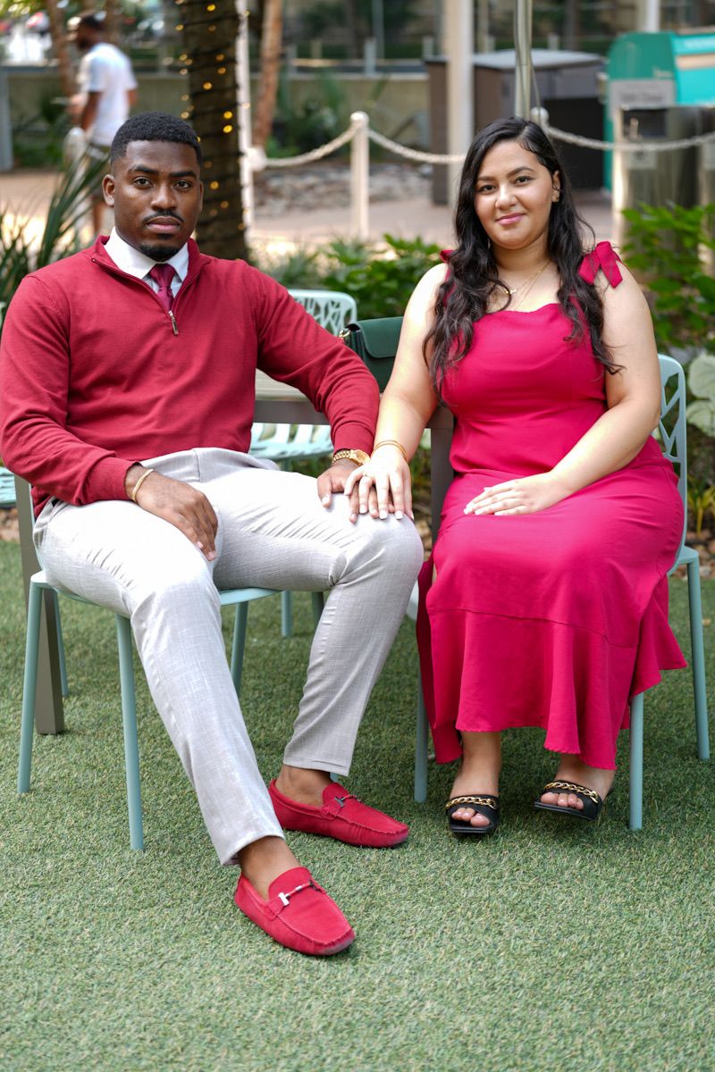 Stylishly dressed couple sits on outdoor patio chairs wearing coordinating red outfits against green turf.