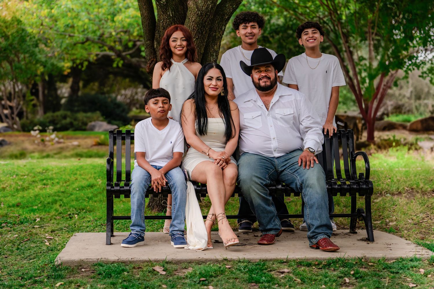 Group portrait of family members sitting together on park bench surrounded by greenery.