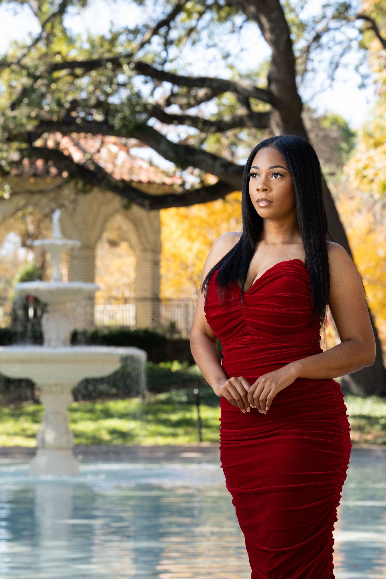 Portrait of a woman in a red dress standing near a fountain at Flippen Park in Highland Park, Texas, captured by DFW Dynamic Media.