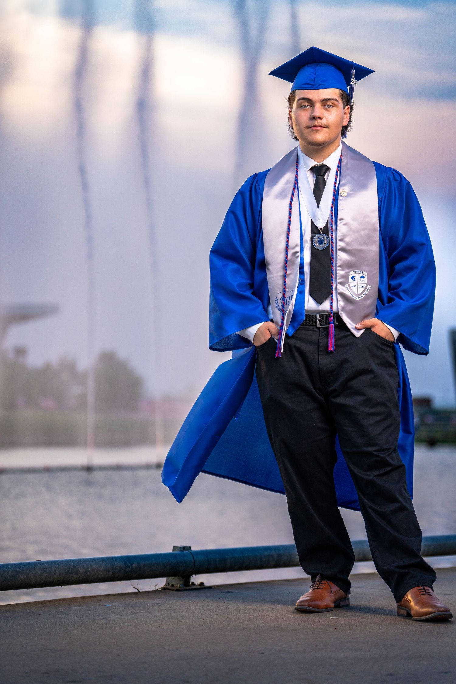 Male college graduate in cap and gown smiling confidently outdoors during golden hour, professional graduation photo in Dallas Texas