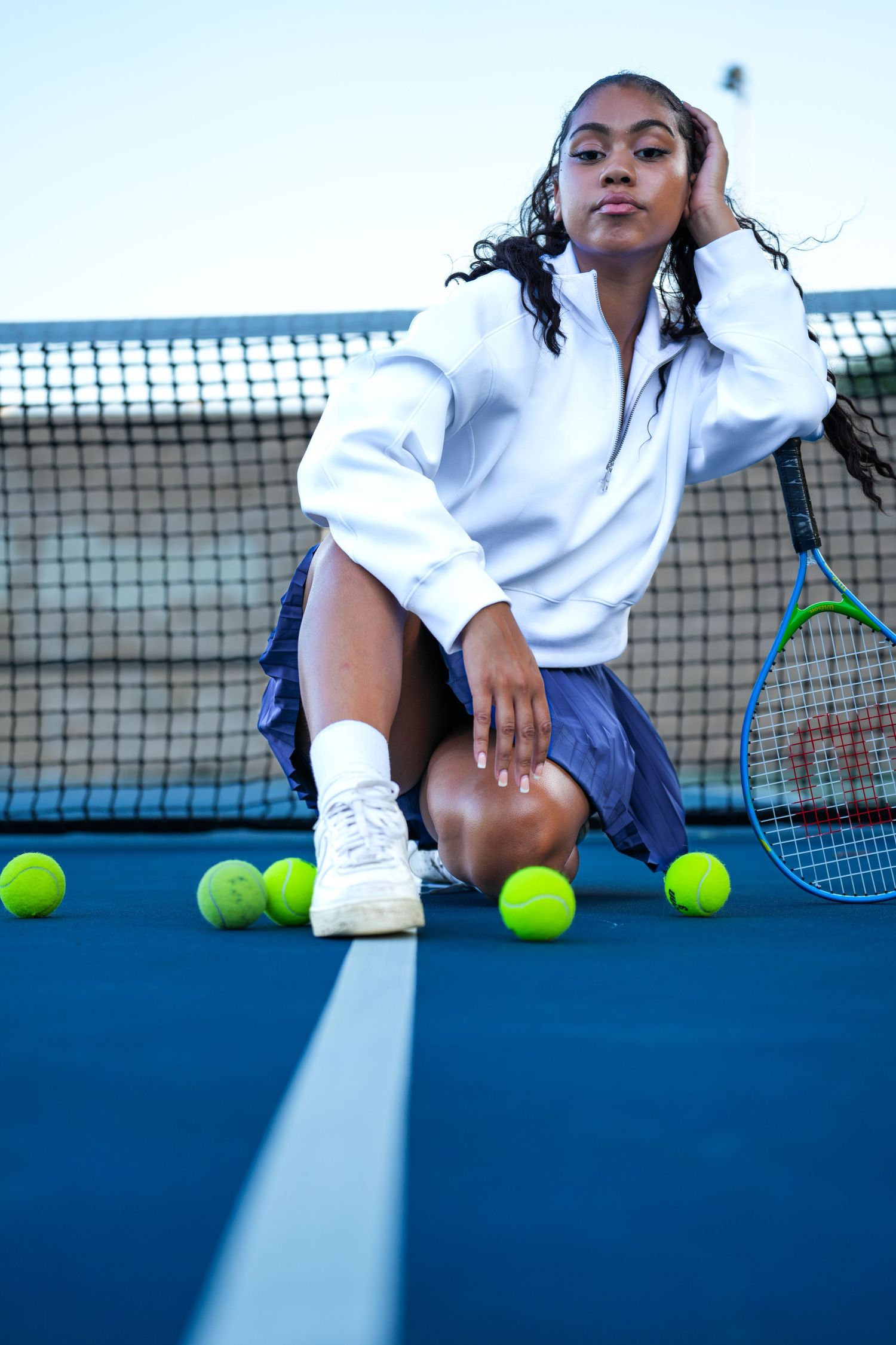 An artistic tennis court photo featuring classic white and navy tennis attire with scattered tennis balls.