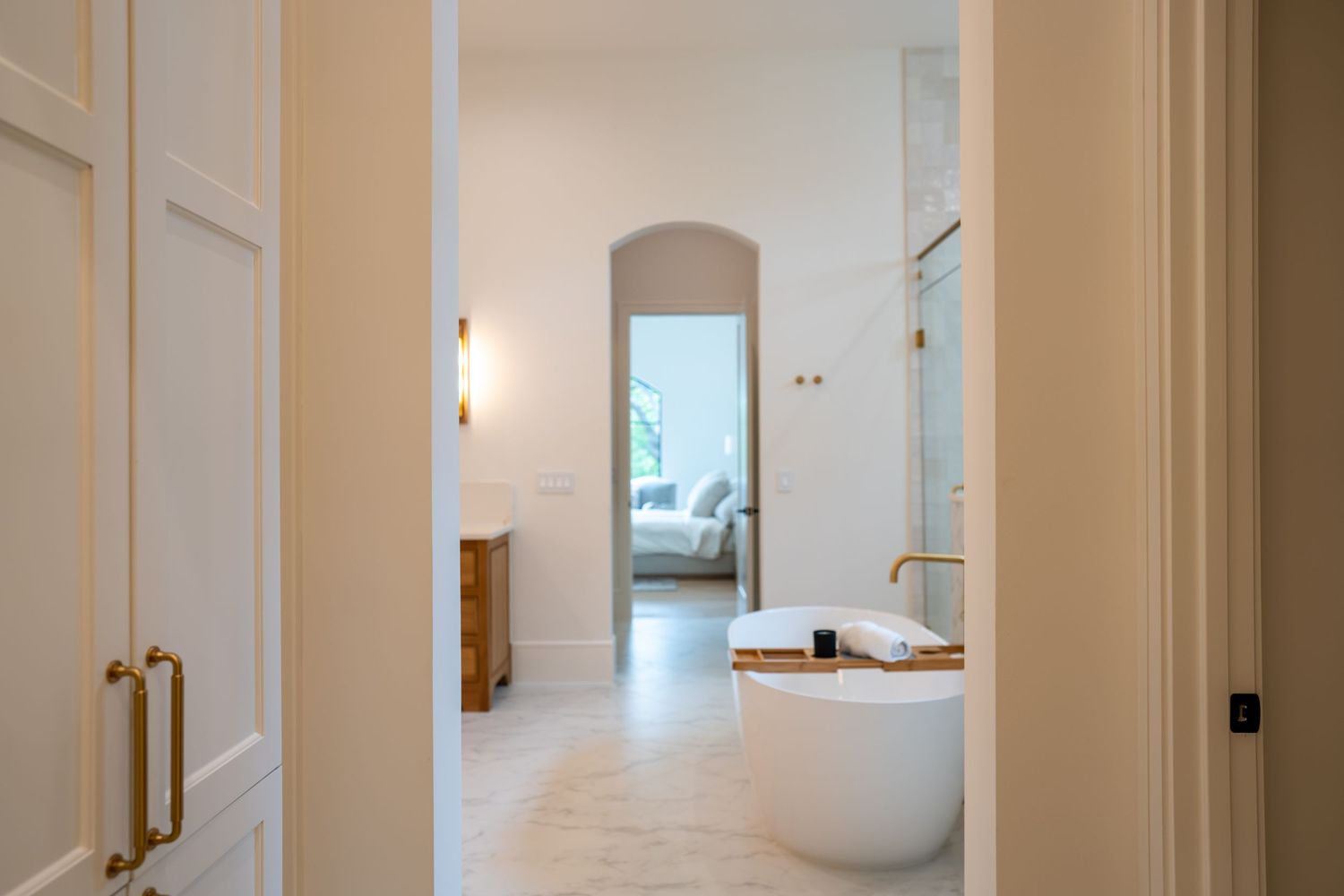 Long hallway view leading to a contemporary bathroom with freestanding tub and natural lighting.