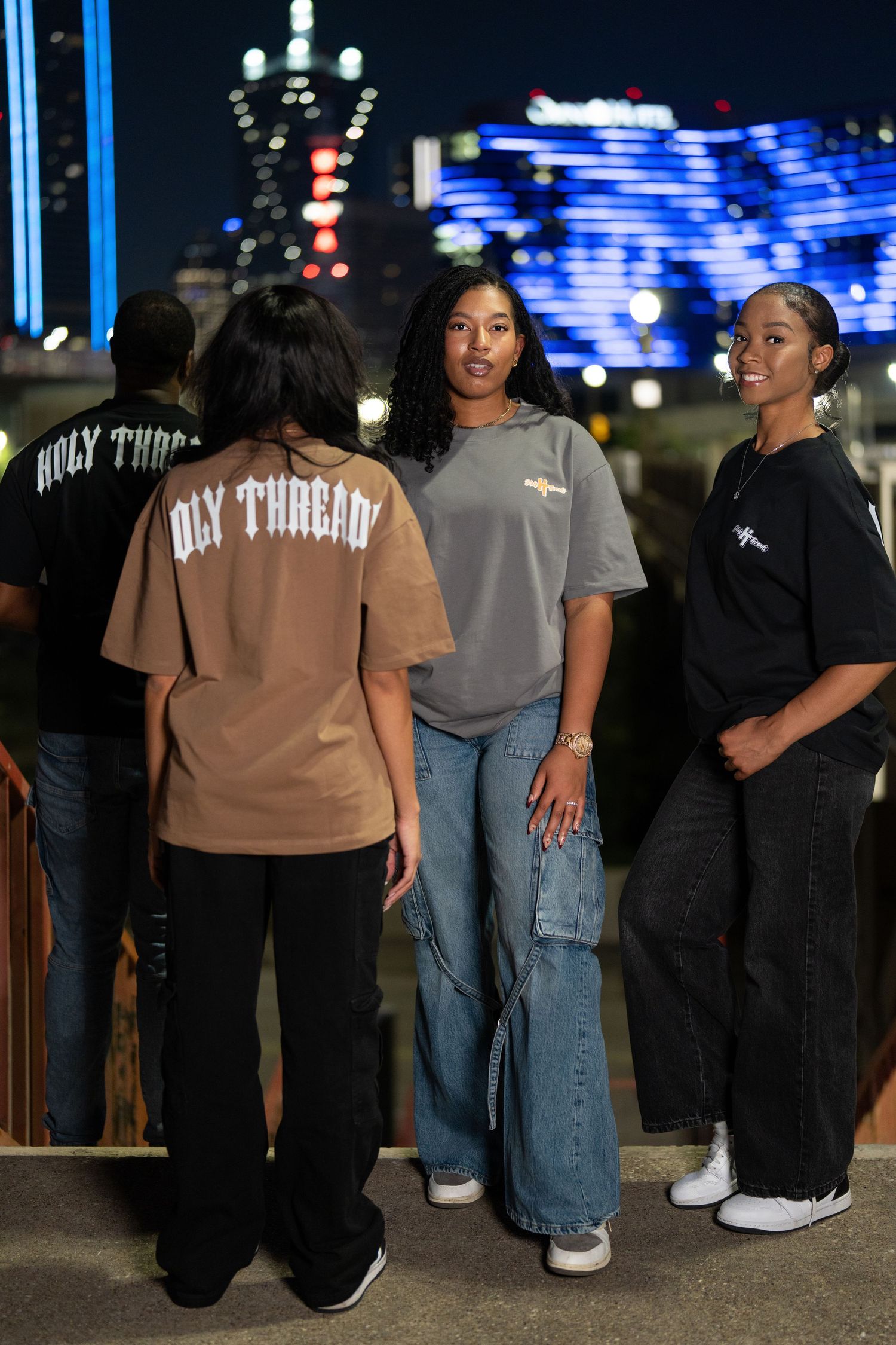 Group wearing casual streetwear standing together at night with illuminated buildings behind them.