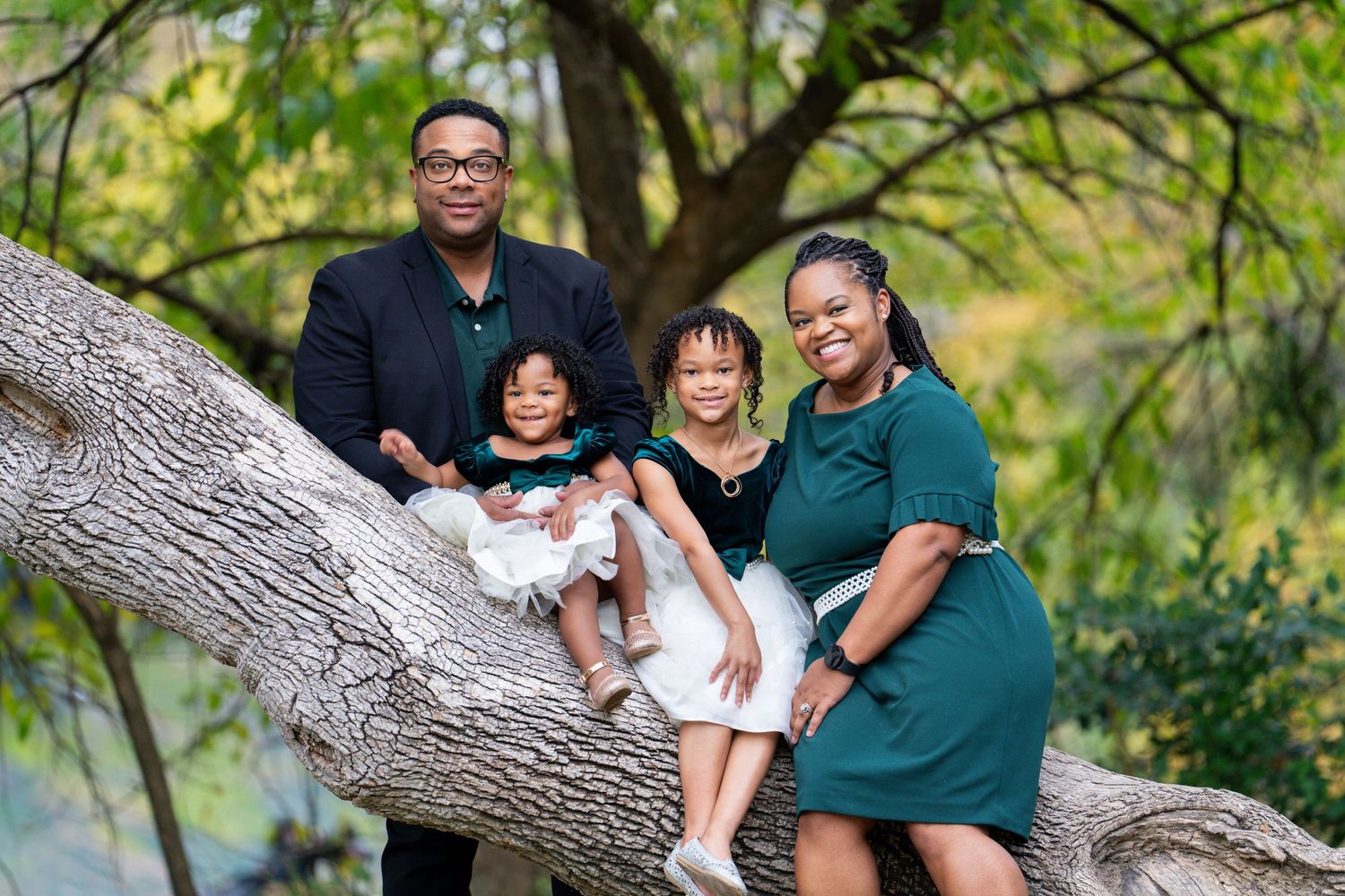 Family posing together on large fallen tree trunk with green foliage background.