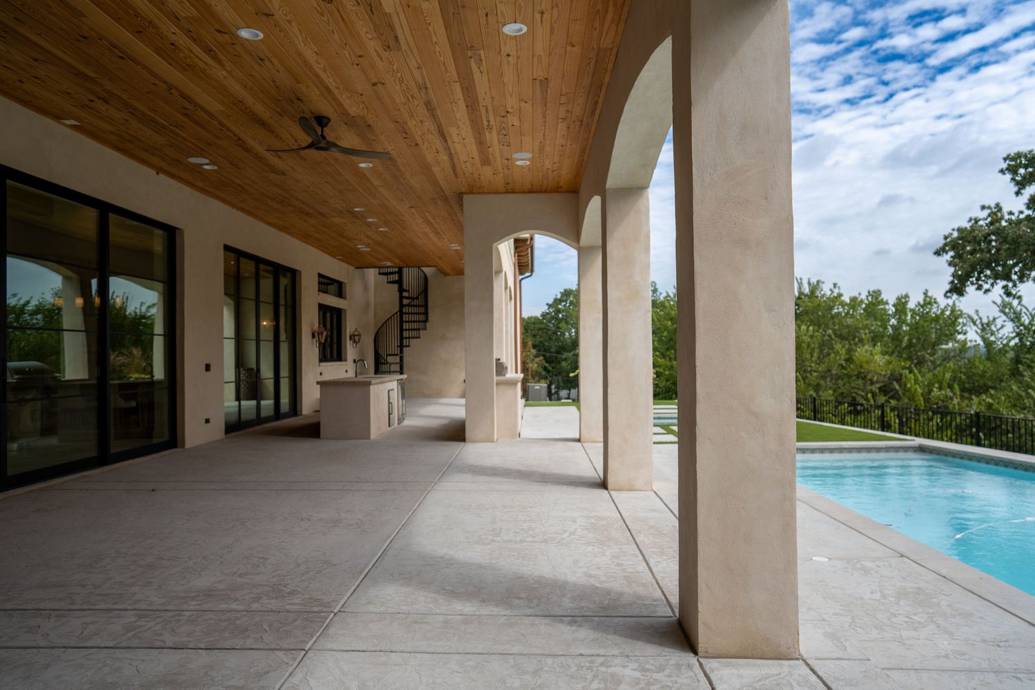 Covered patio with stone columns and wood ceiling overlooking a swimming pool.