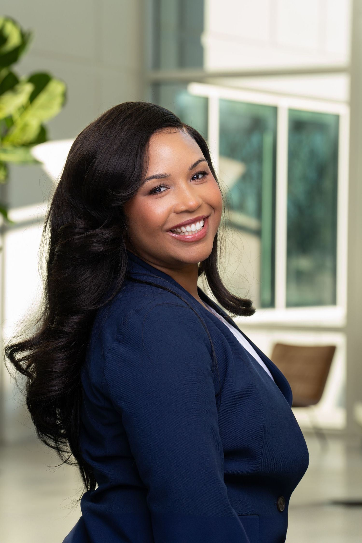 A professional in a navy blazer poses confidently in a modern office environment.