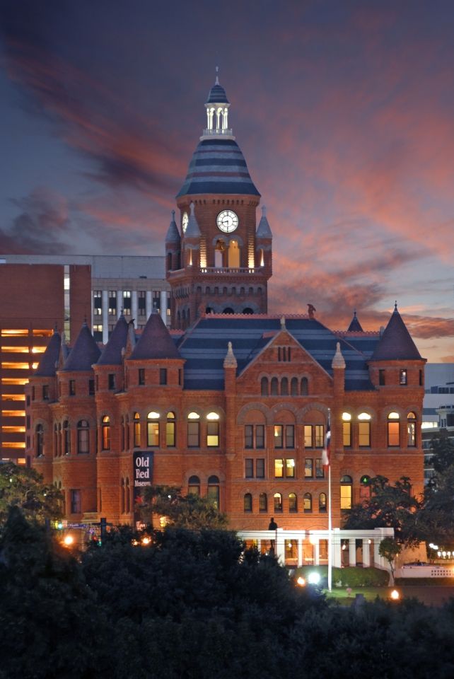 Historic red brick Victorian-style courthouse building illuminated at dusk with dramatic orange and purple sunset sky.