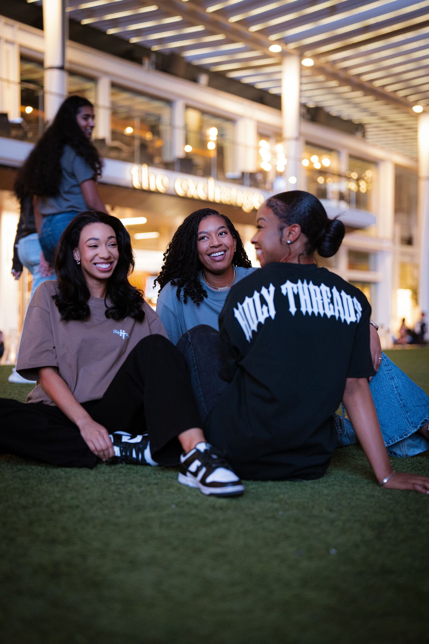 Group relaxing on grass wearing Holy Threads apparel during evening.