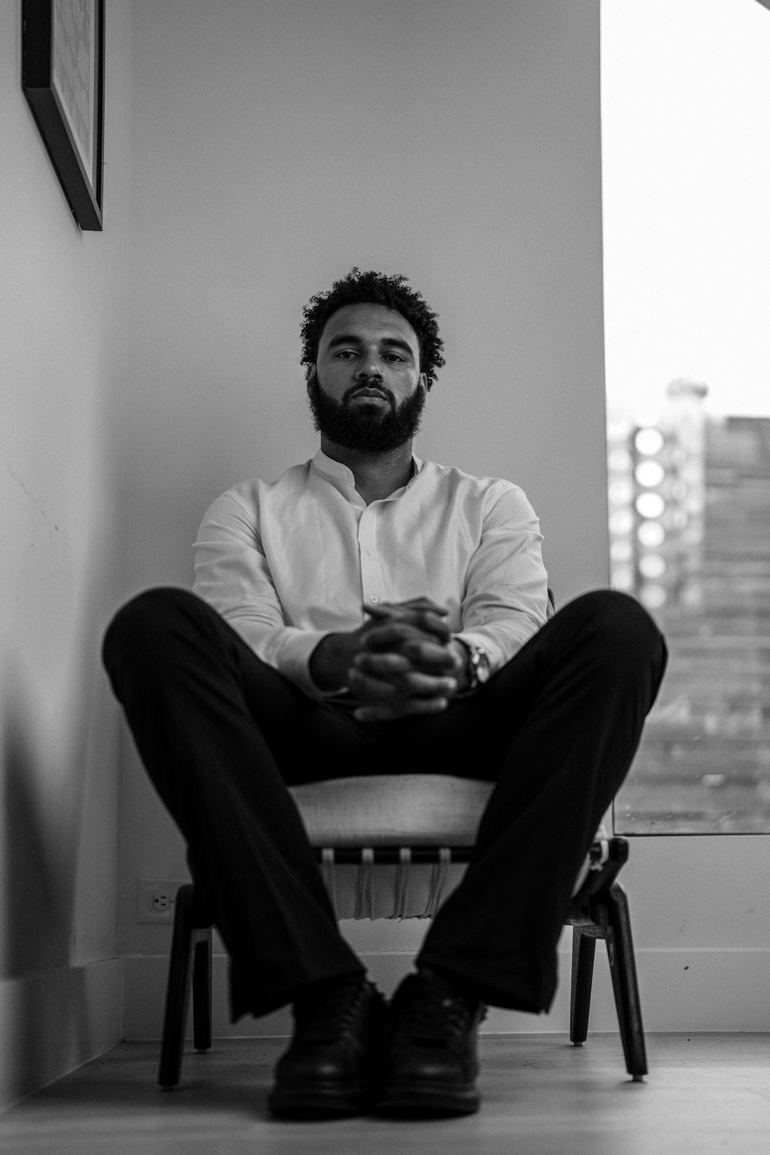 Black and white portrait showing relaxed seated pose against minimal background.