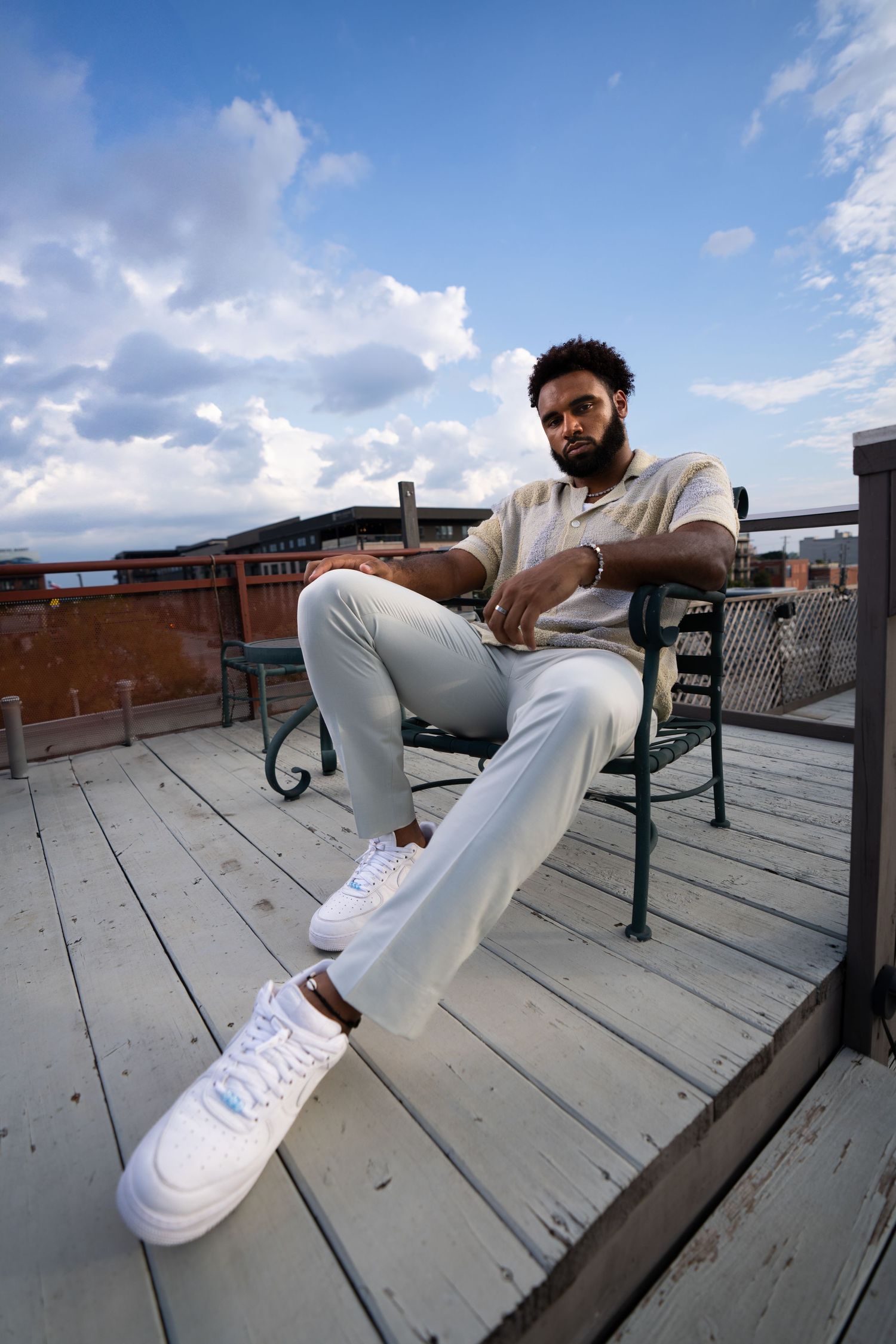 Urban portrait session on rooftop deck with casual white outfit and sneakers against cloudy sky background.