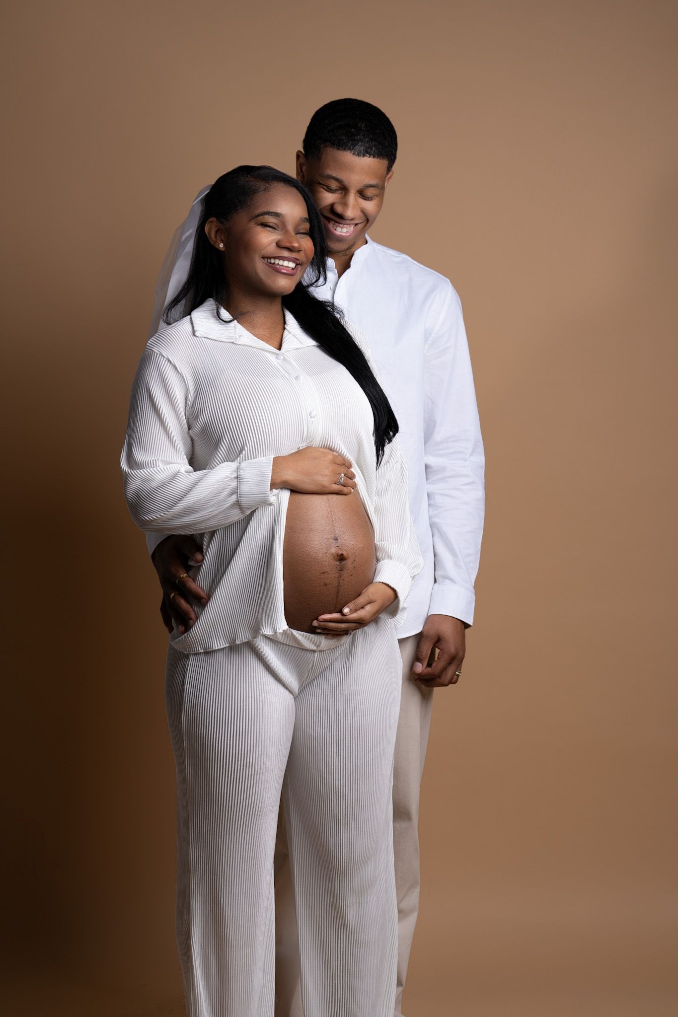 A series of intimate maternity photos showing a couple in all-white clothing against a brown background.