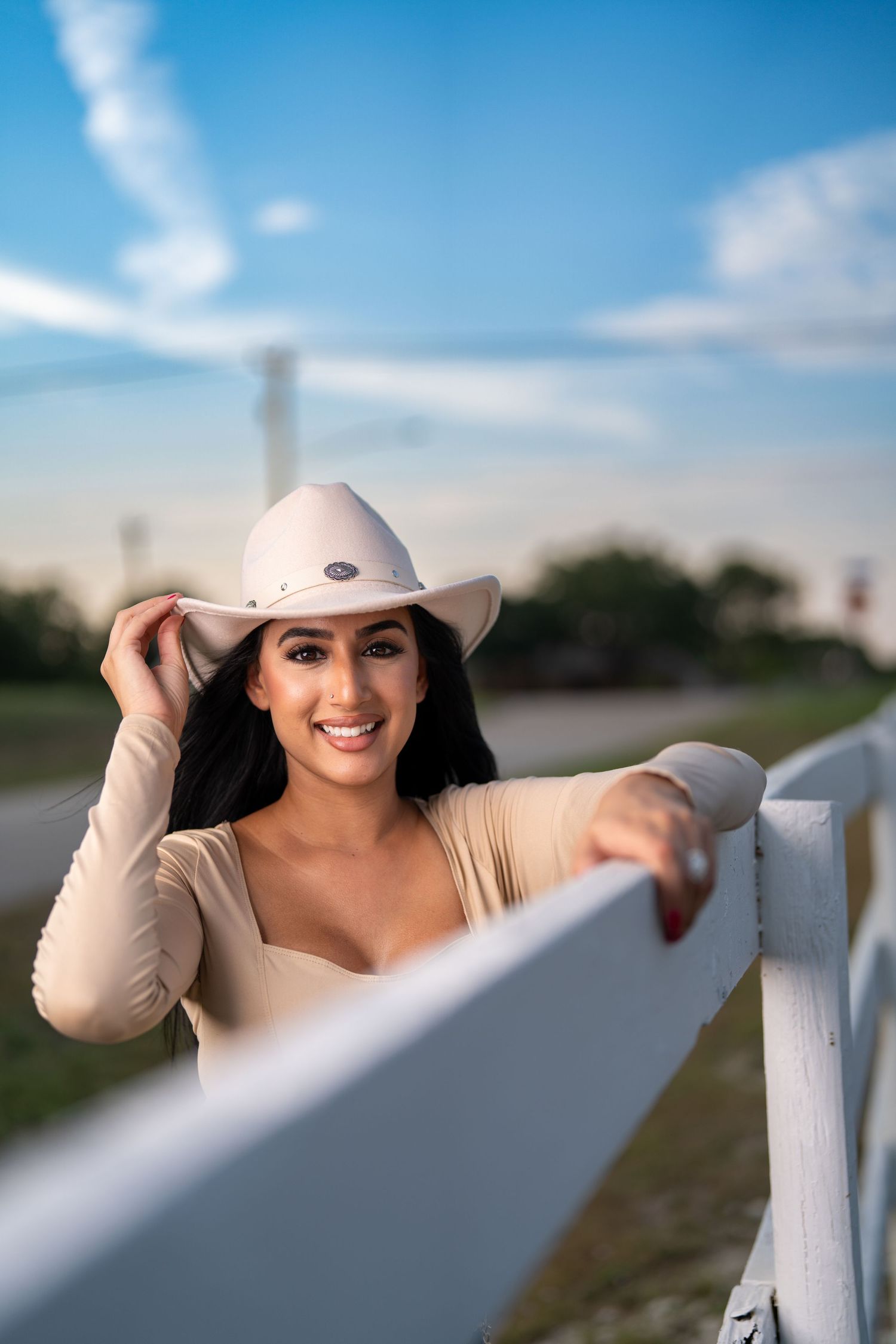 Casual western portrait leaning on white fence under bright blue sky.