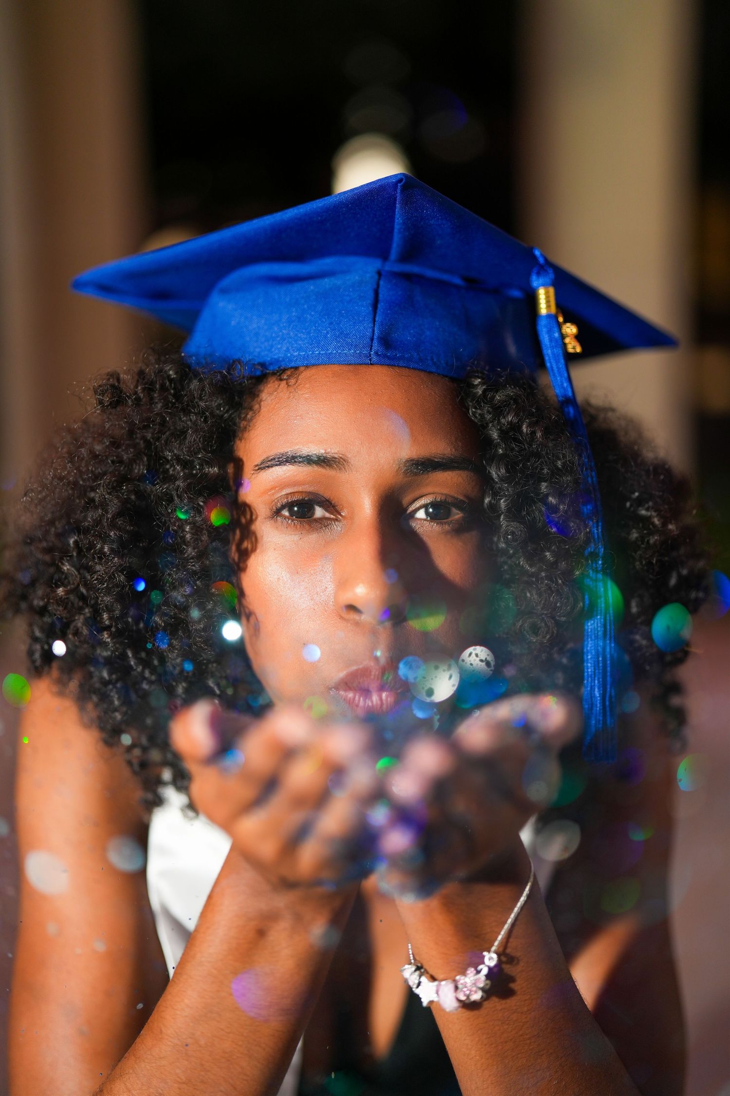 Graduate in blue cap blowing glitter while celebrating commencement.
