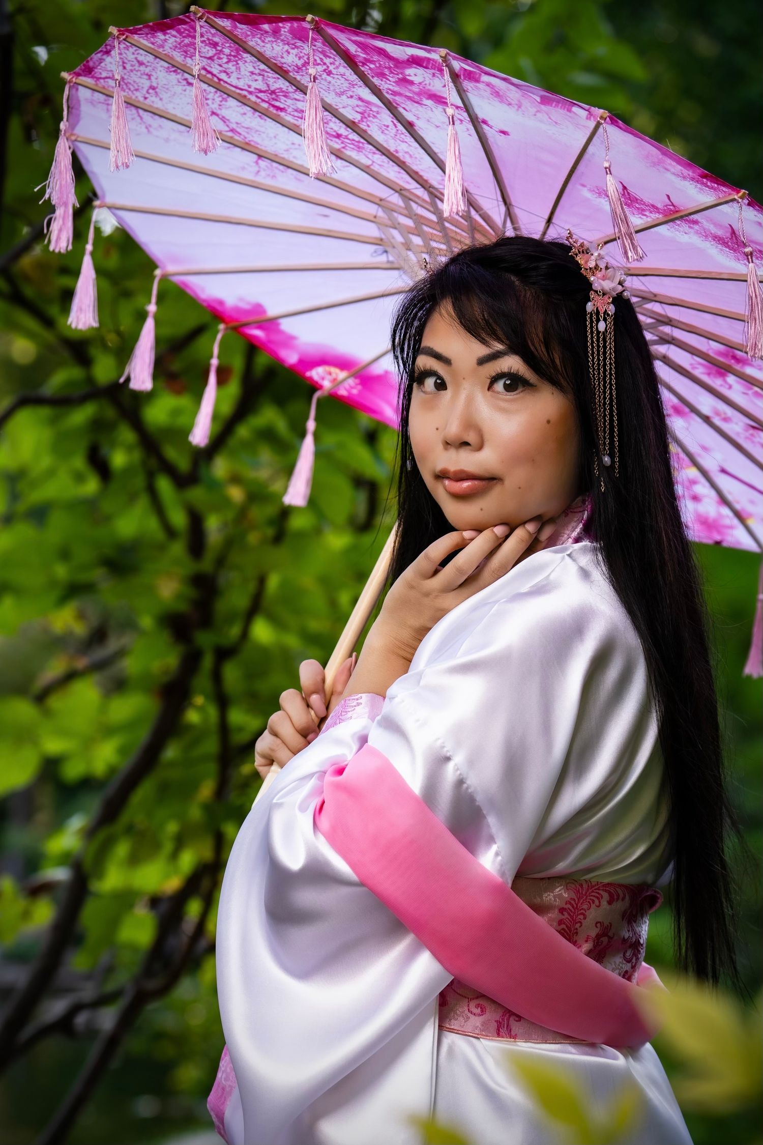 Traditional Japanese parasol adds a delicate pink accent against lush green foliage background in garden setting. DFW Portraits.