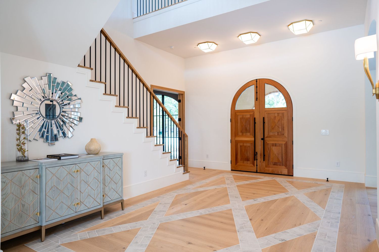Grand foyer with wooden double doors, patterned marble floors, and decorative staircase.
