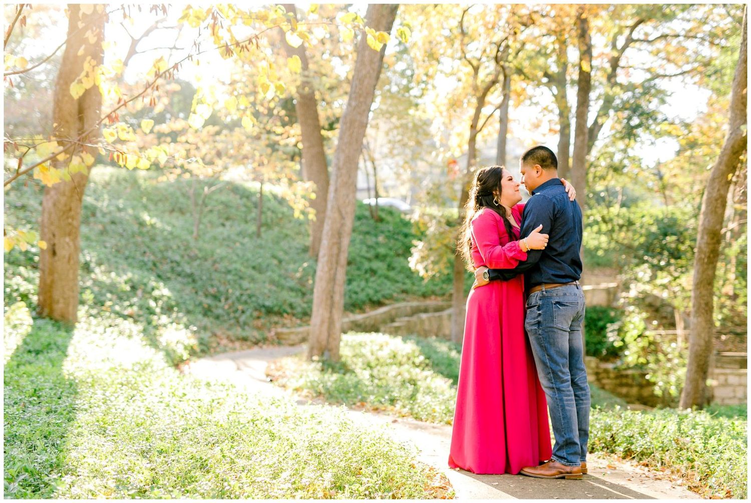 Serene forest scene with couple in bright pink dress and navy suit embracing during golden hour photography session.