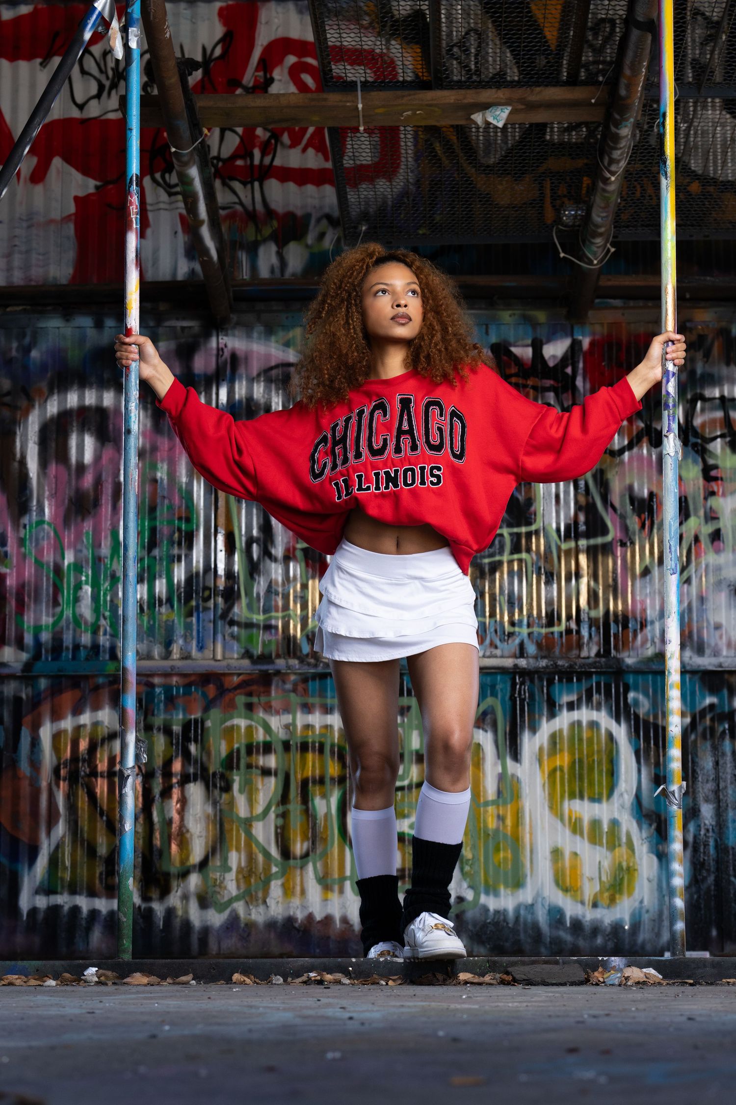 A sequence of playful sidewalk photos showing a person in a red Chicago sweatshirt swinging by metal poles with graffiti walls.