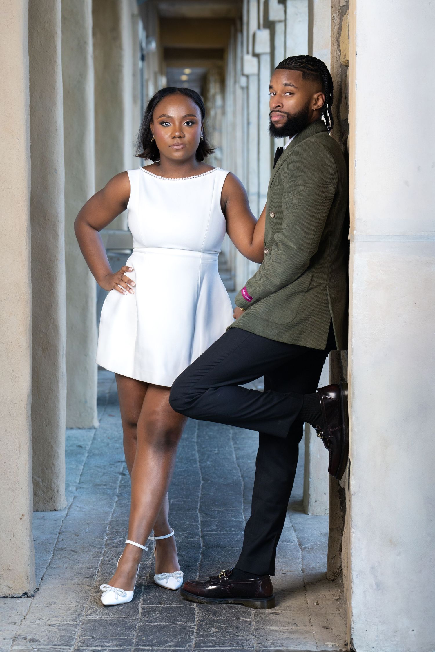A couple poses confidently in a covered walkway wearing coordinated formal attire.