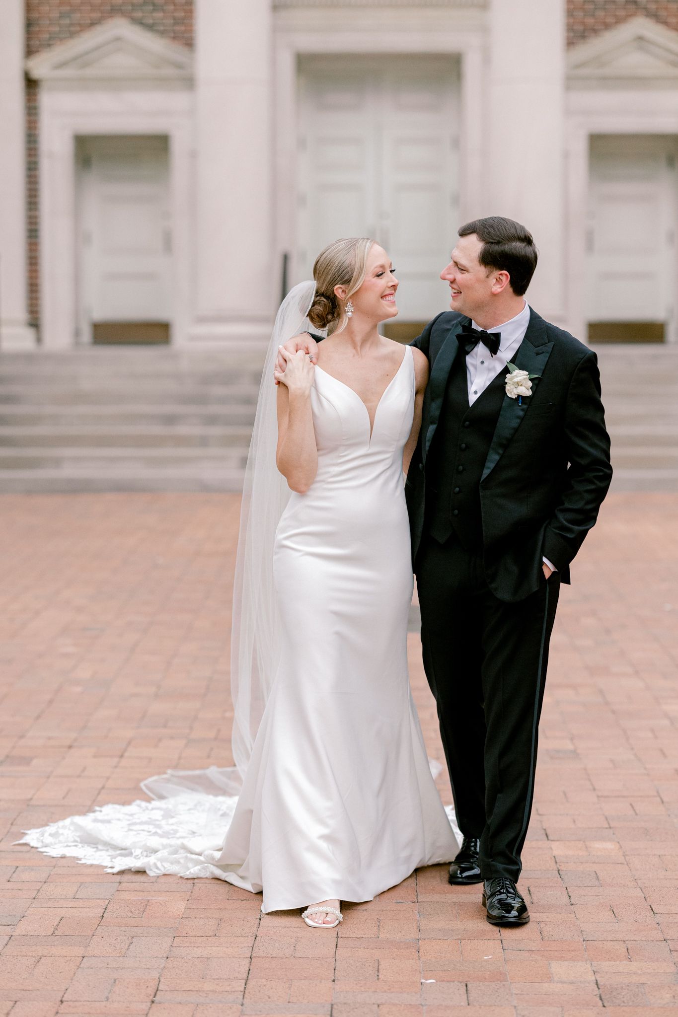 Newlywed couple sits and shares romantic moments on brick courtyard in elegant wedding attire.