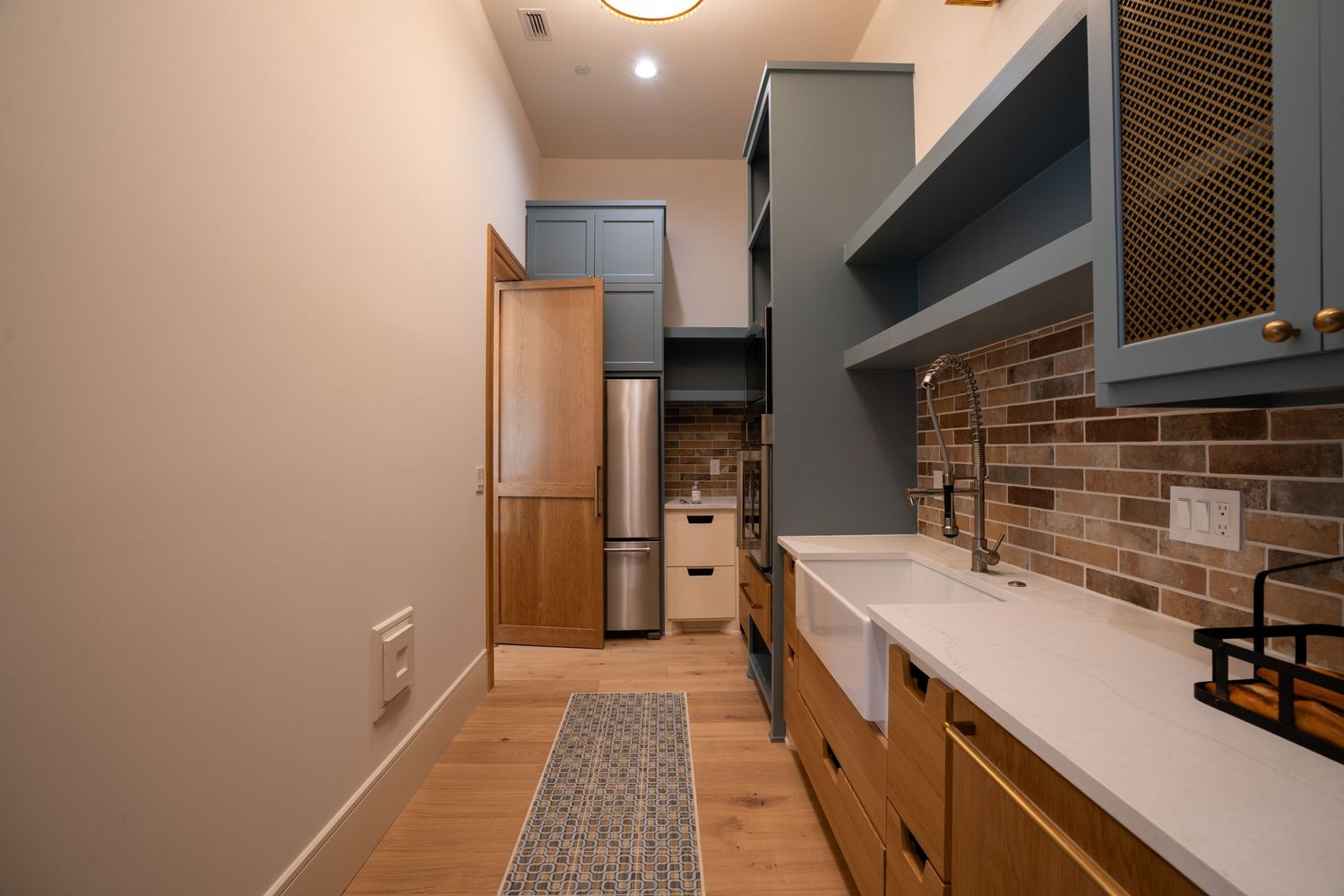 Modern galley kitchen with wood cabinets, white countertops and patterned runner.