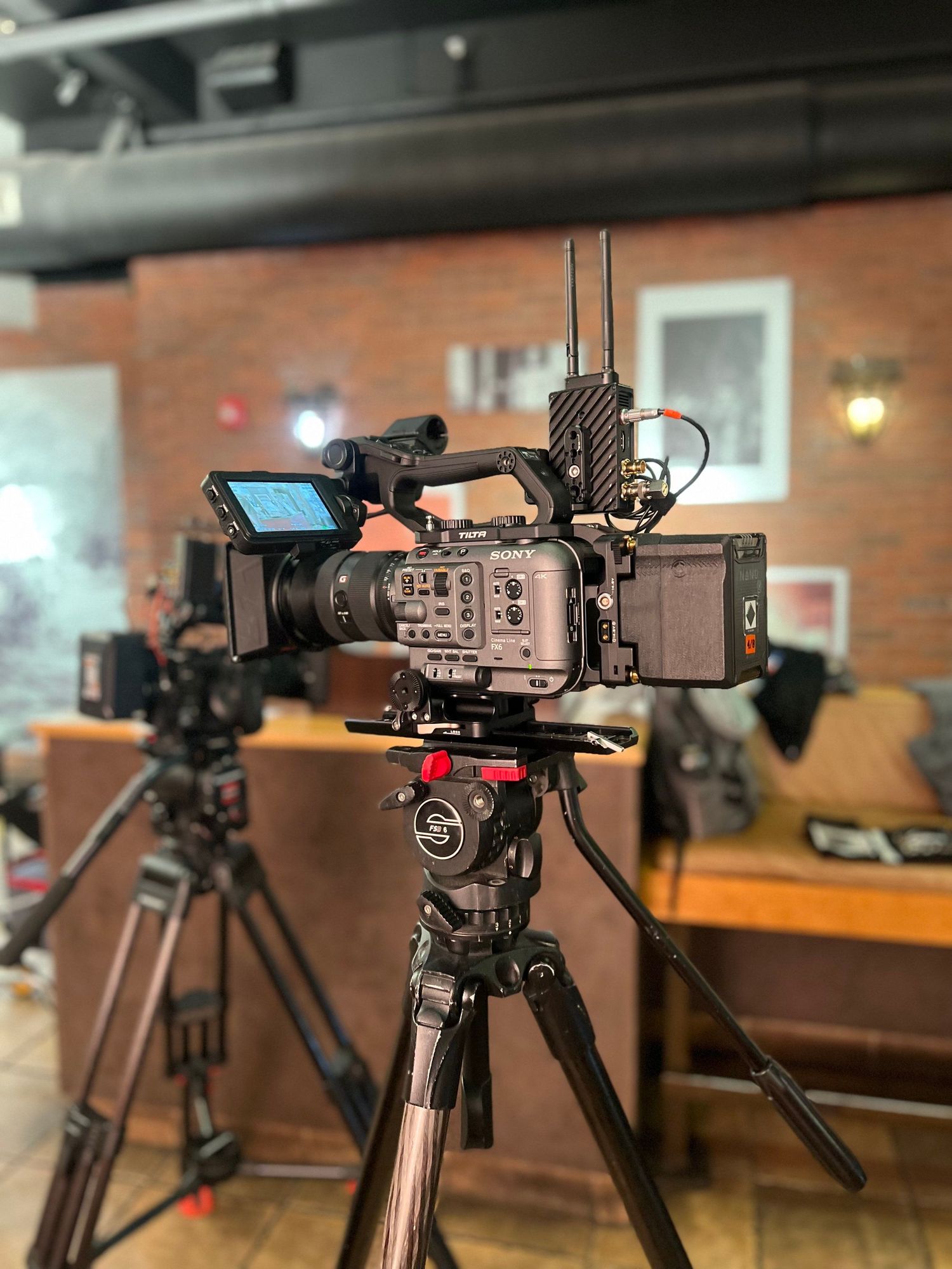 Professional video camera mounted on tripod with monitor display in brick-walled studio setting.