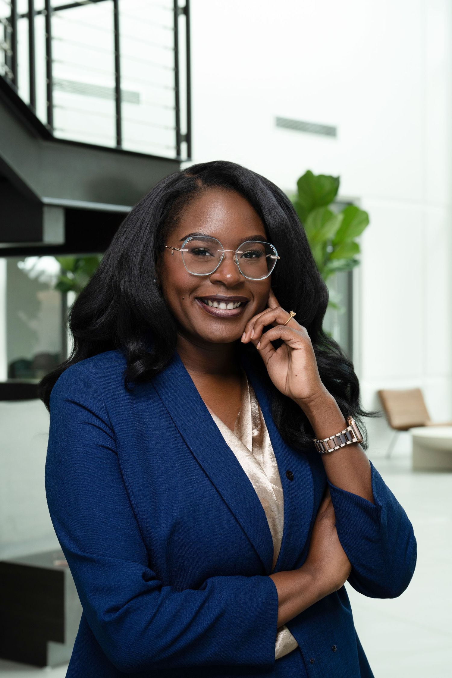 Professional in navy blazer and glasses poses confidently in modern office interior.