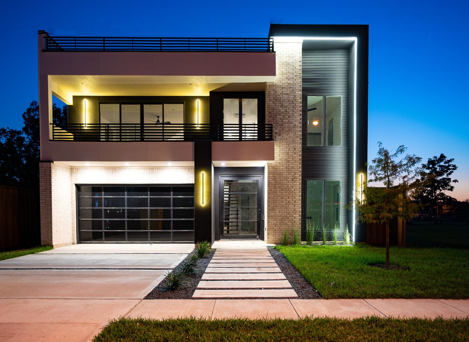 Modern two-story house with glass walls and contemporary architecture illuminated at dusk.