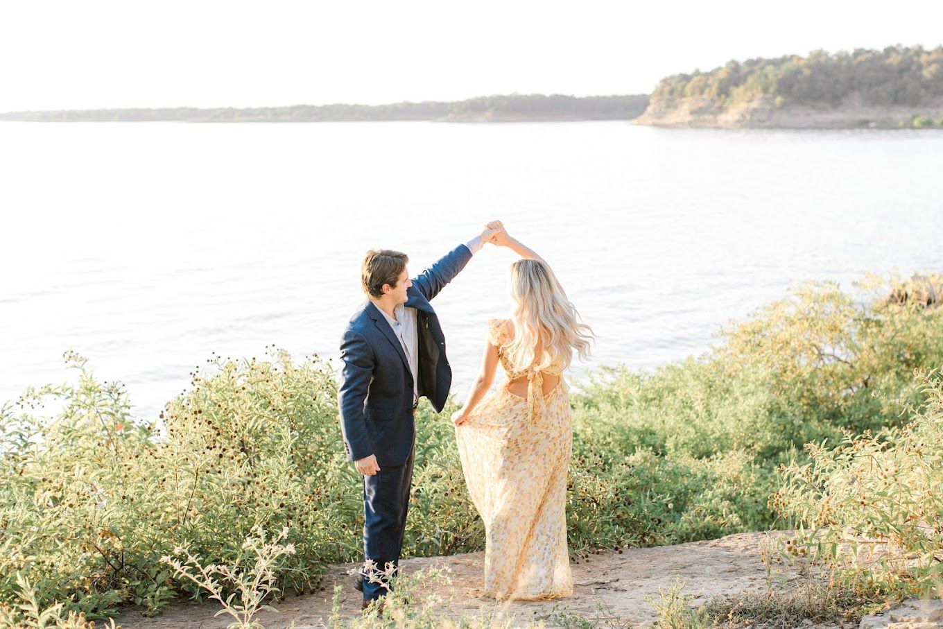 A couple in formal attire walks along a scenic coastal cliff during golden hour.