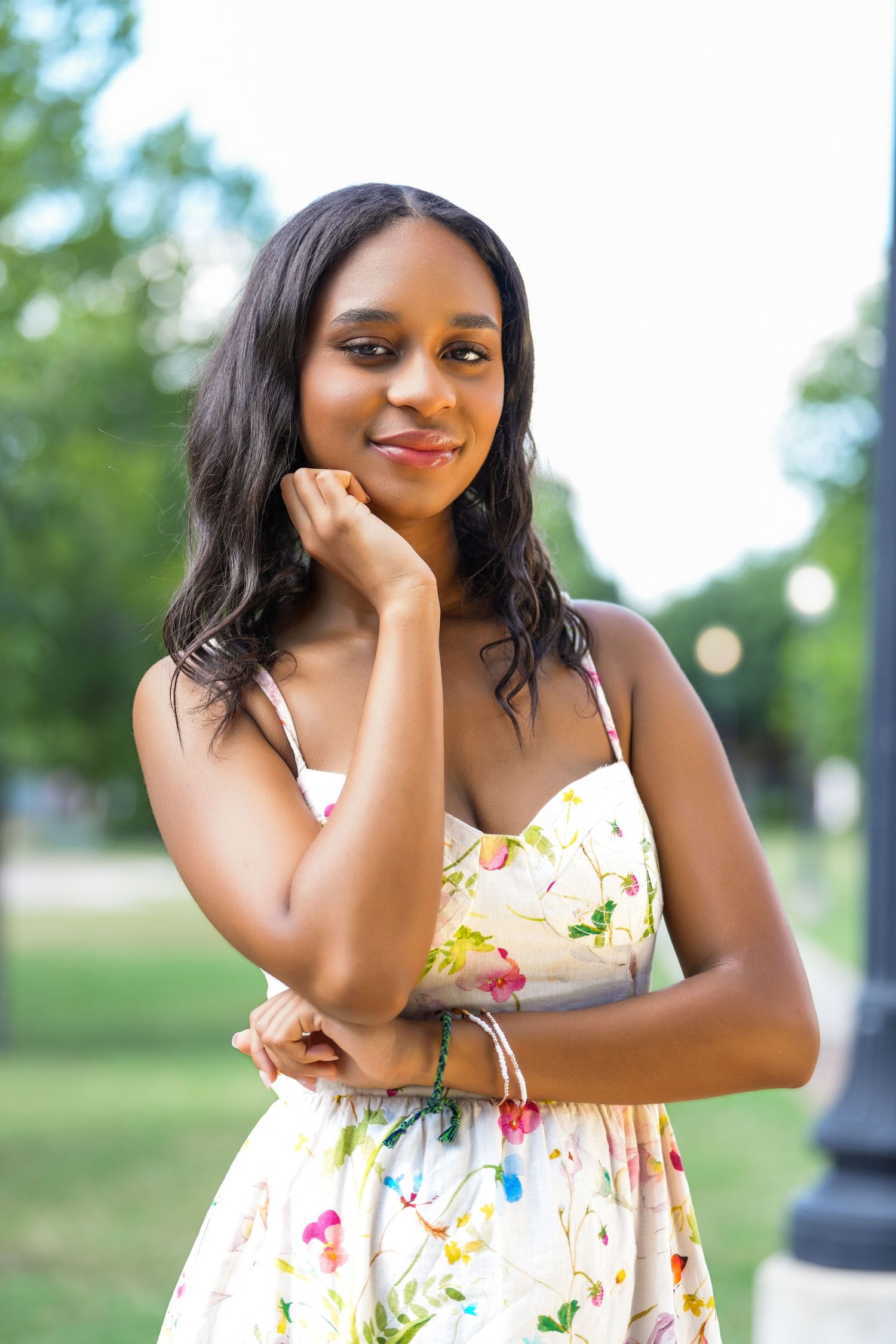Elegant pose in floral sundress against blurred green park background.