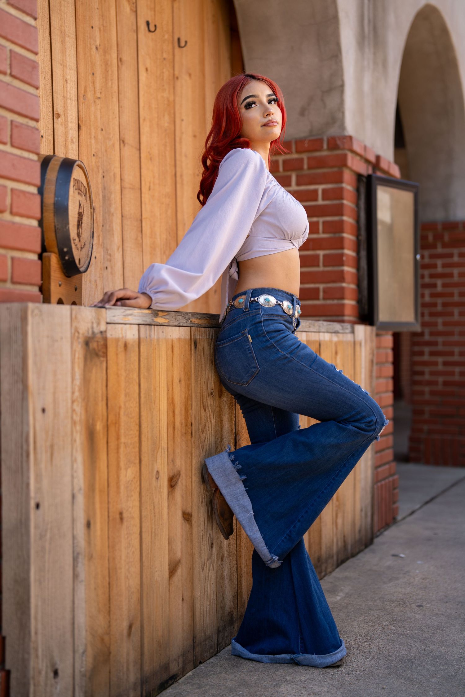 Retro-inspired fashion look with bell bottom jeans and cropped blouse against wooden door.