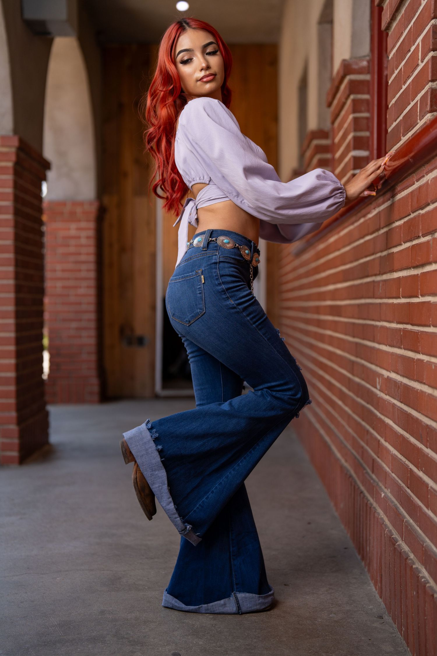 Fashion model in purple crop top and flared jeans poses in brick archway.